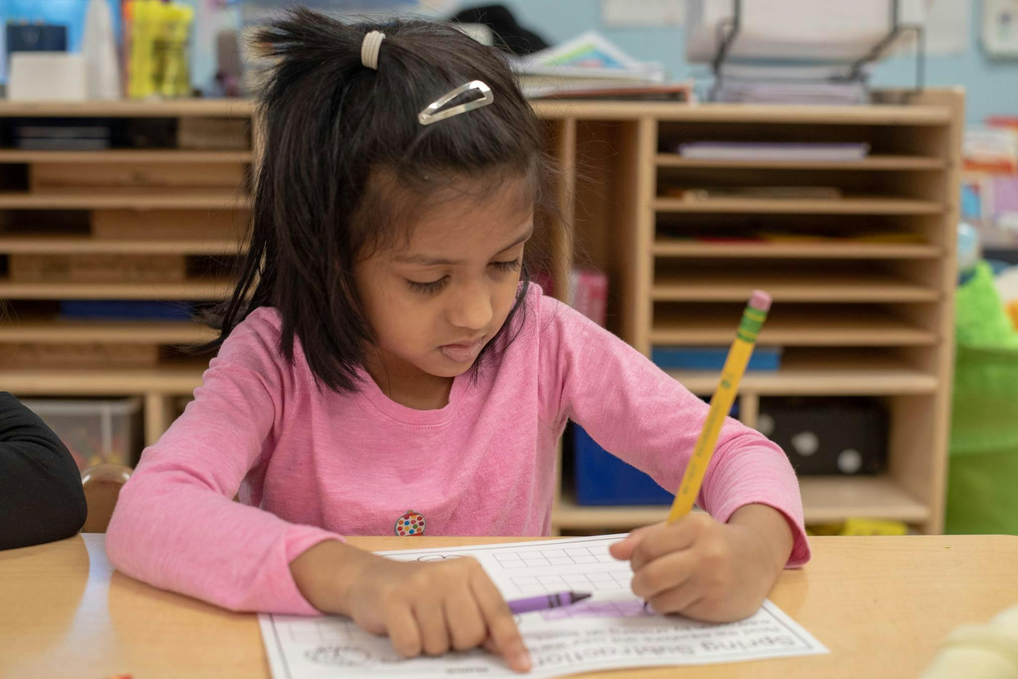 Child writing on paper with a pencil in a classroom