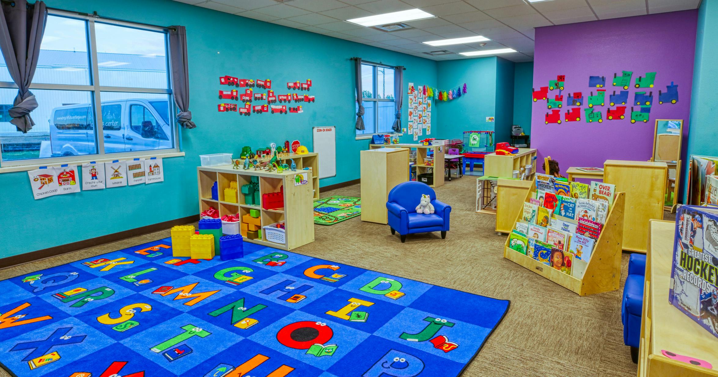 Classroom with blue walls, children's furniture, an alphabet rug, and toys
