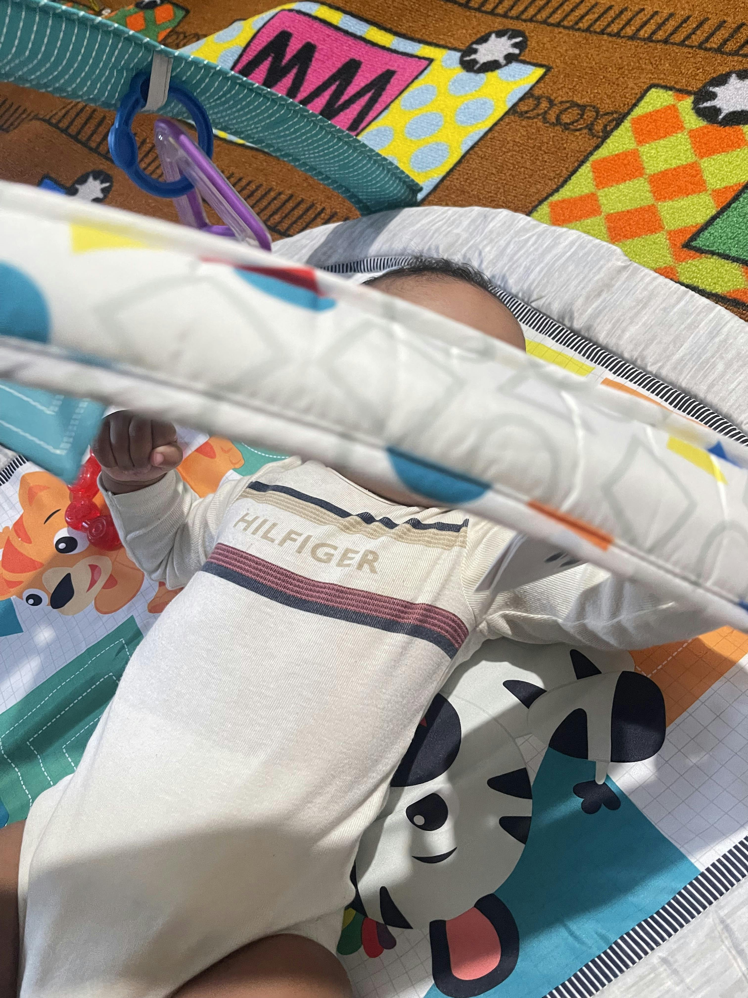Child lying on a play mat with 'HILFIGER' written on their shirt