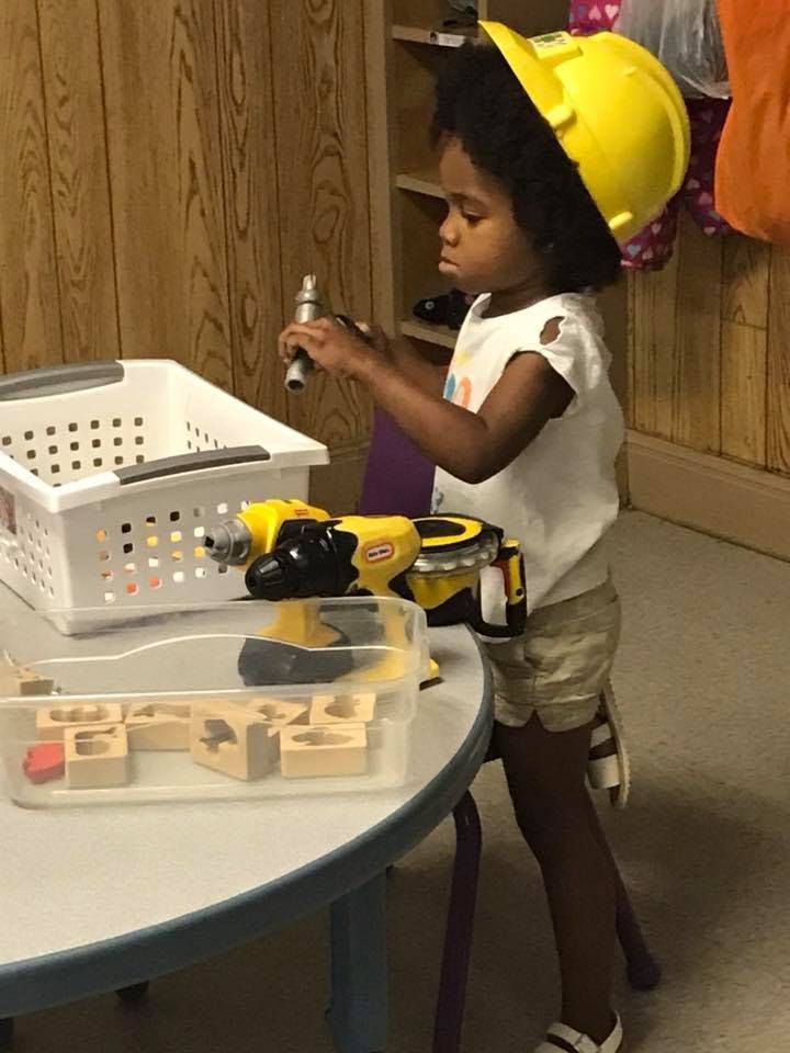 Child in a yellow hard hat holding a toy tool