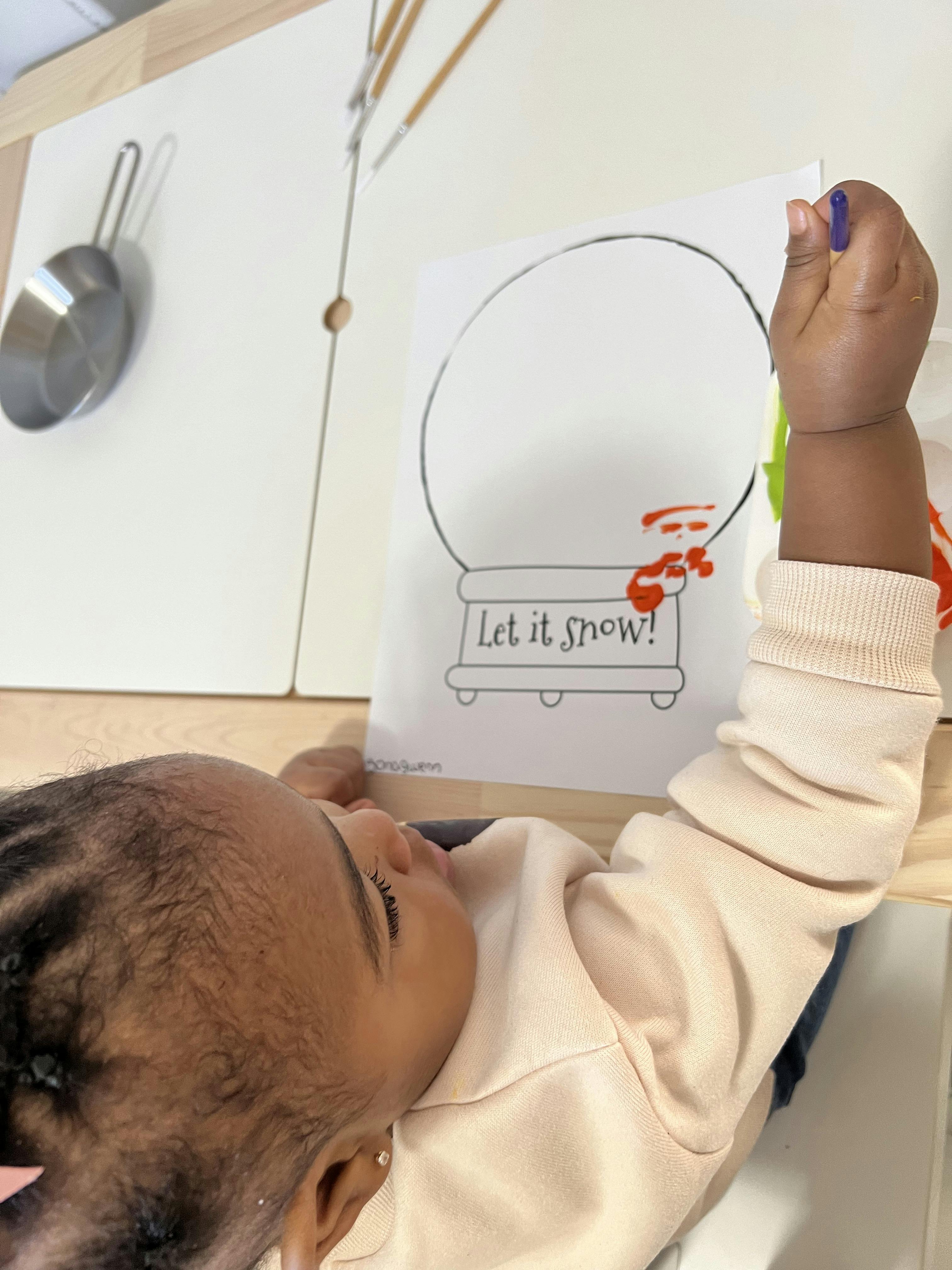Child coloring a snow globe worksheet that says Let it snow