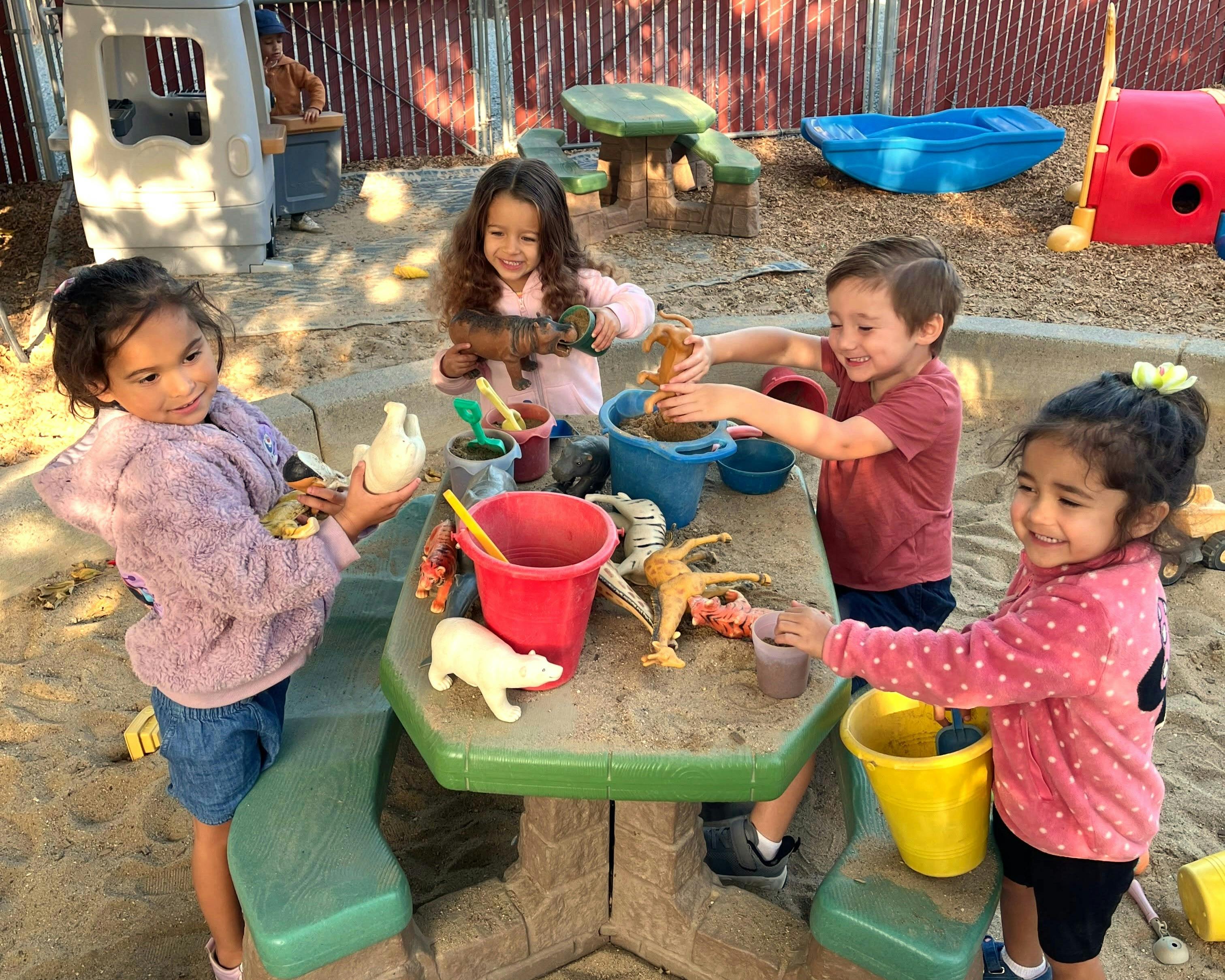 Four children playing with toy animals at a sandbox table