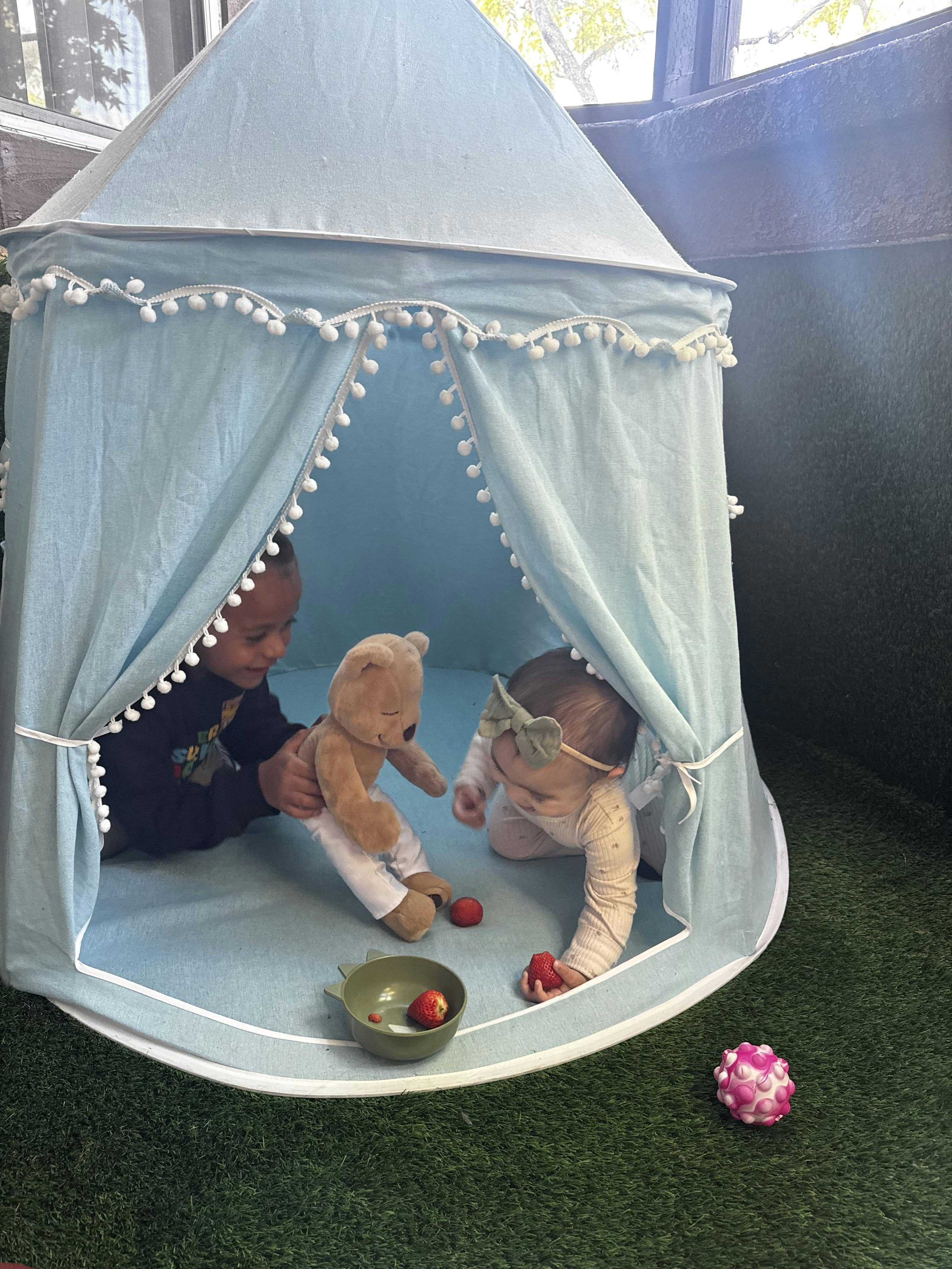 Child playing with a teddy bear and baby crawling with strawberries in a tent