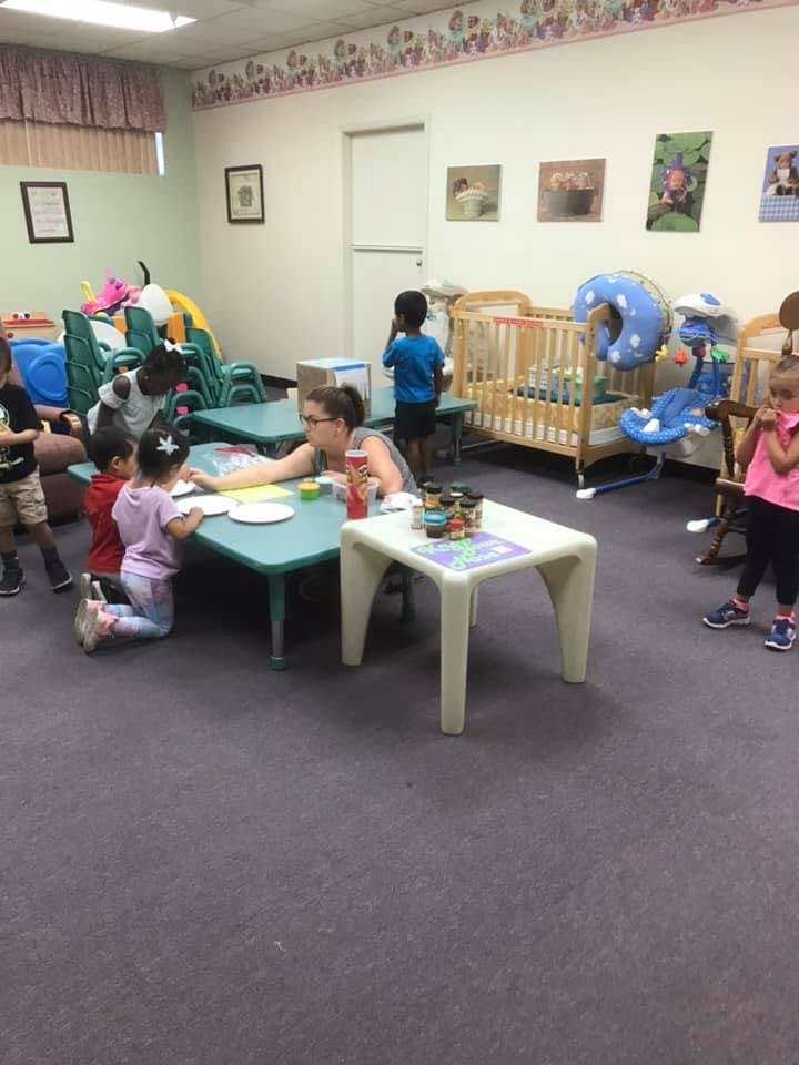 Adult and children at tables in a room with cribs