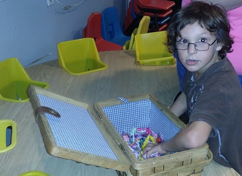 Child with glasses reaching into a basket filled with candy