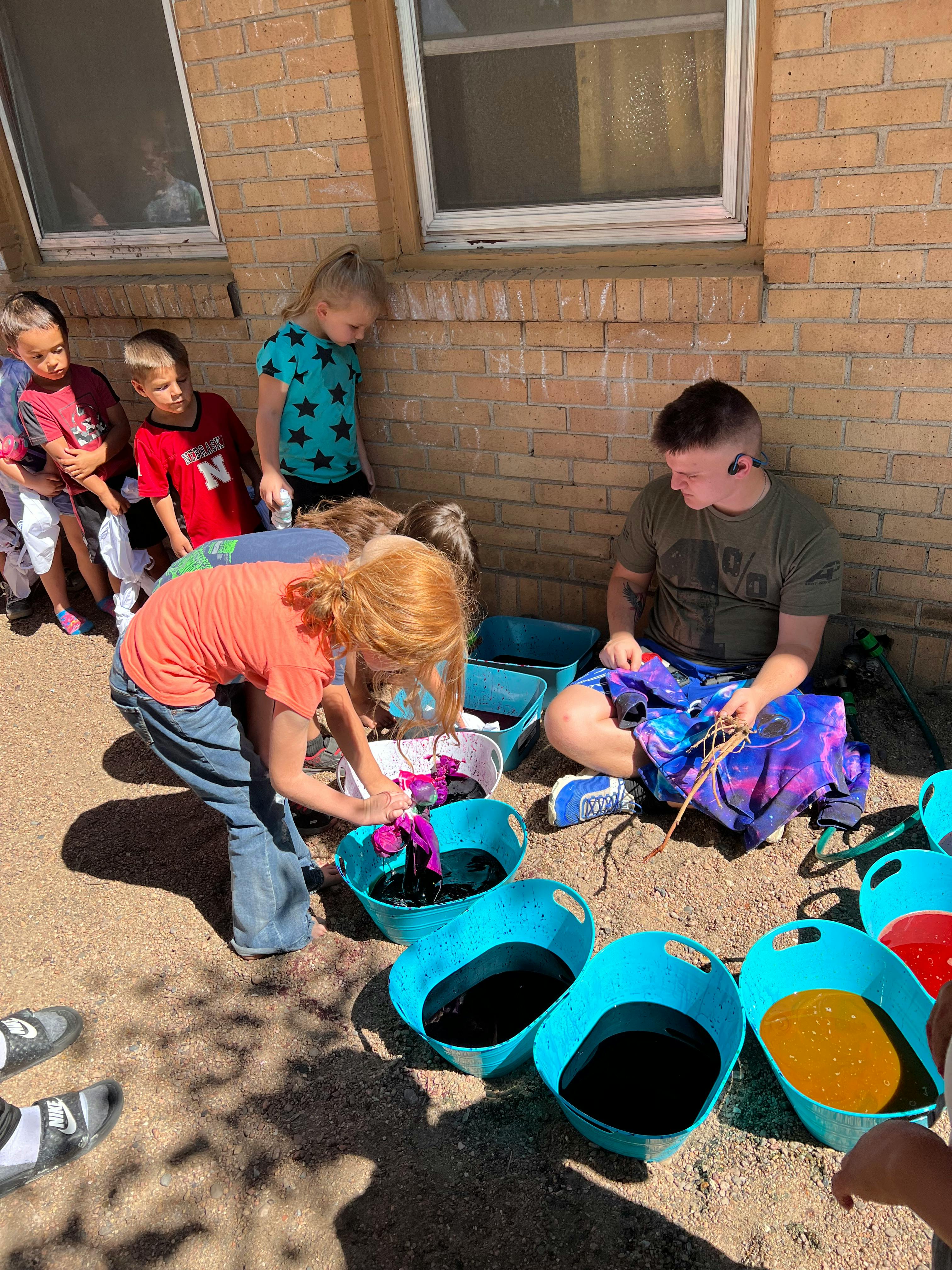People tie-dyeing outdoors with buckets of colored liquid