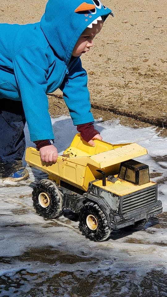 Child in a blue hooded jacket playing with a yellow toy dump truck