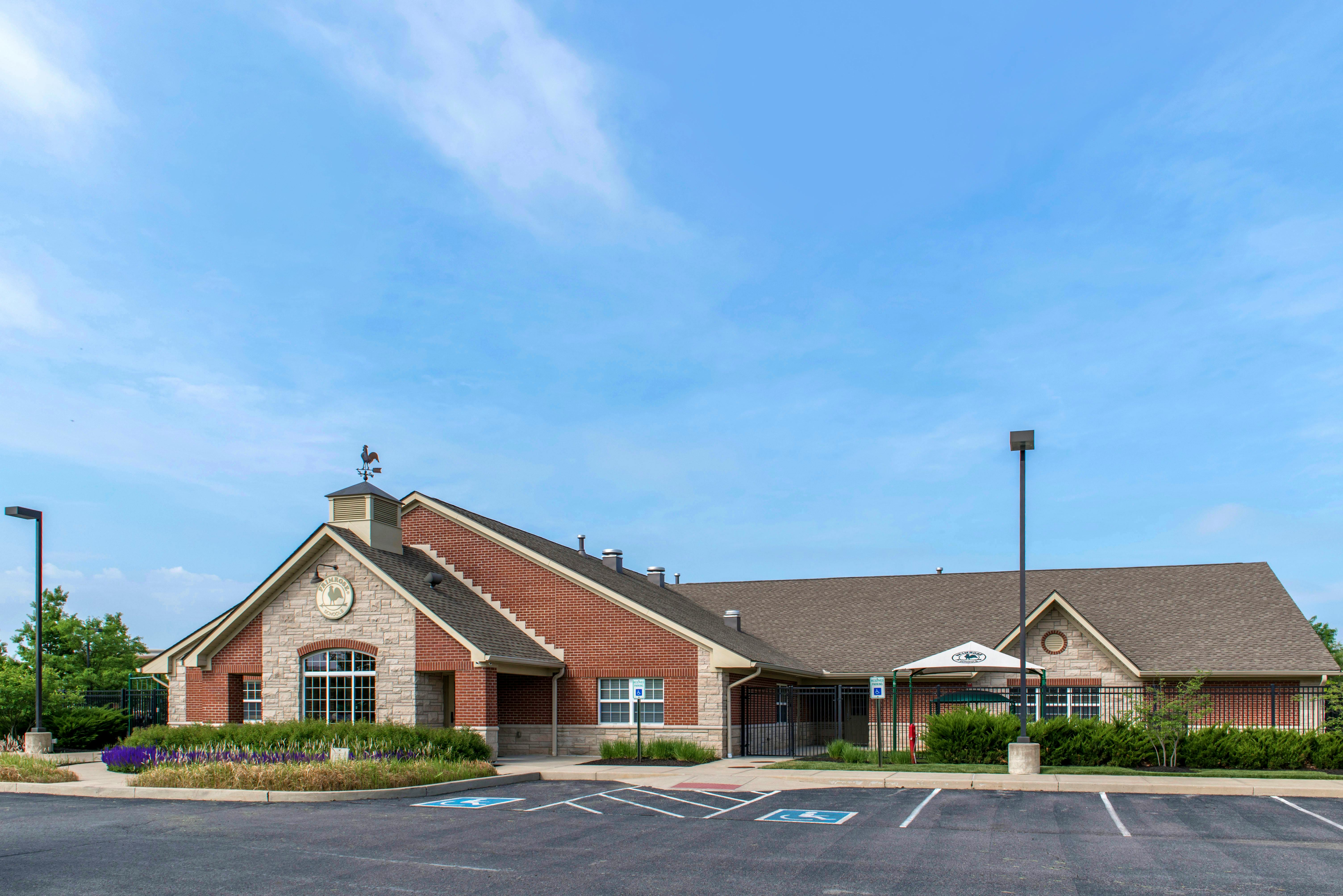 A brick and stone building with a rooster weathervane on the roof, next to a parking lot