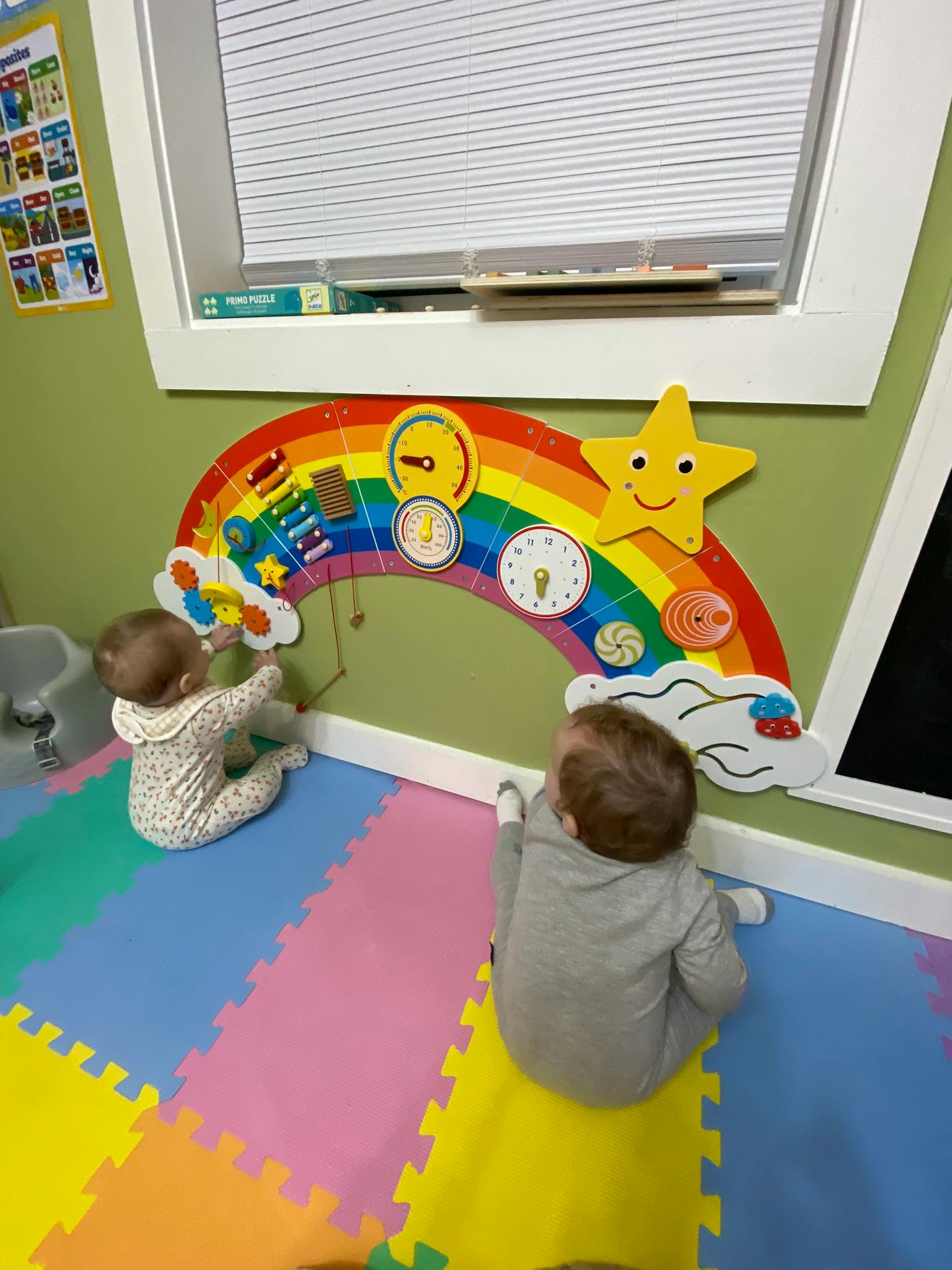 Two children playing with a rainbow-shaped activity board