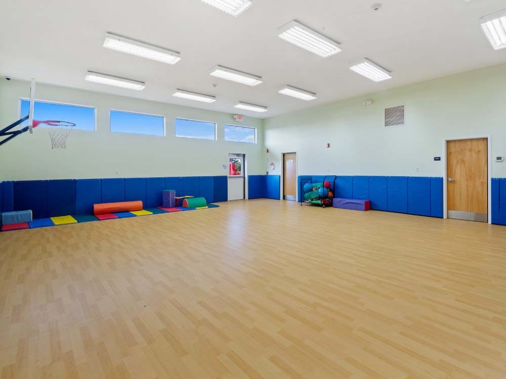 Indoor gym with basketball hoop, colorful mats, and wall padding