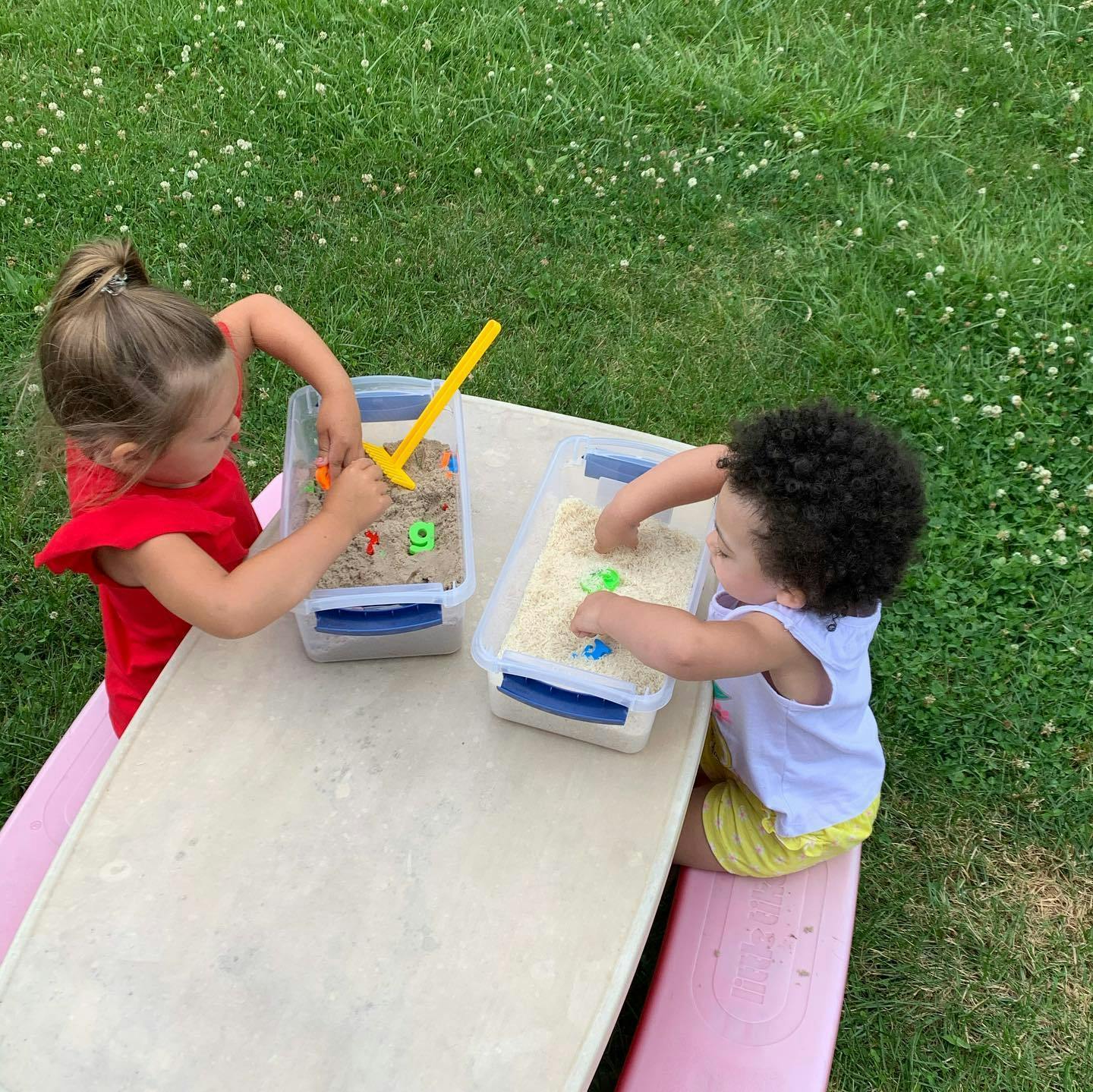 Two children playing with sand and toys in containers on a table