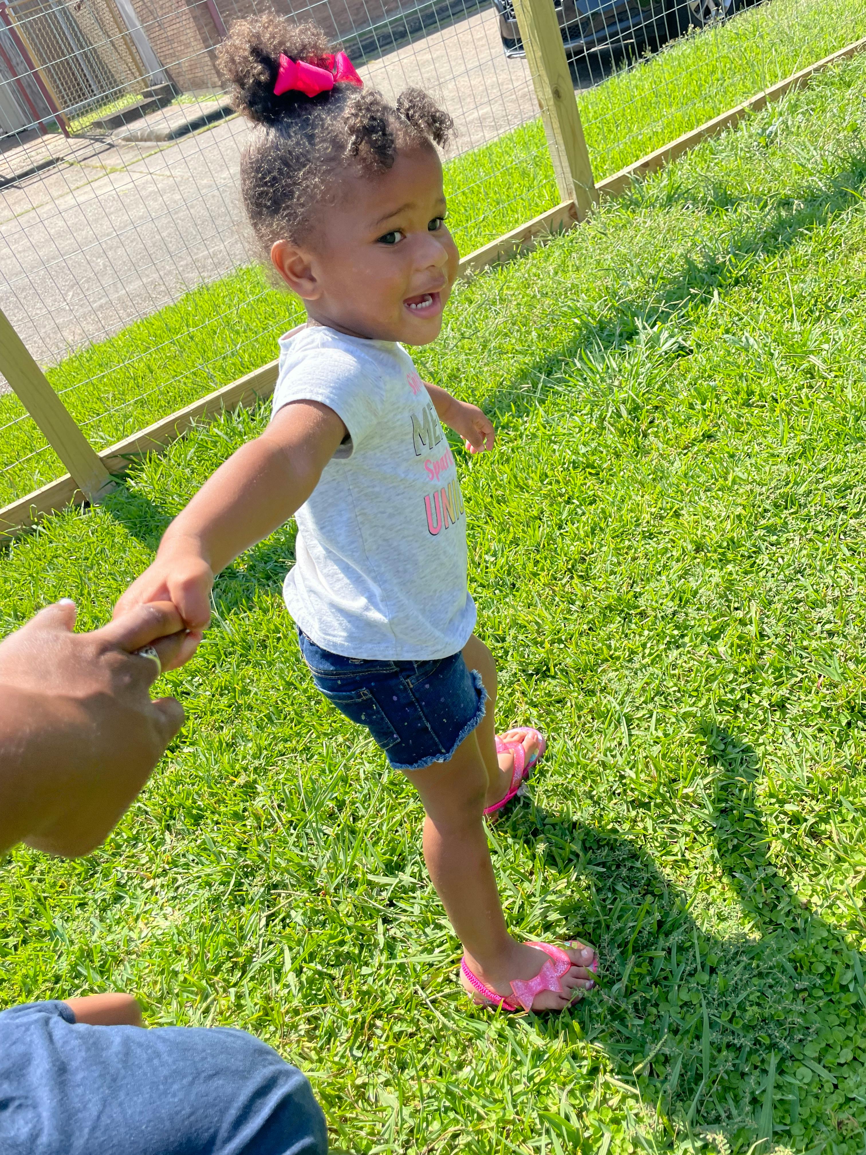 Child holding a person's hand and walking on grass