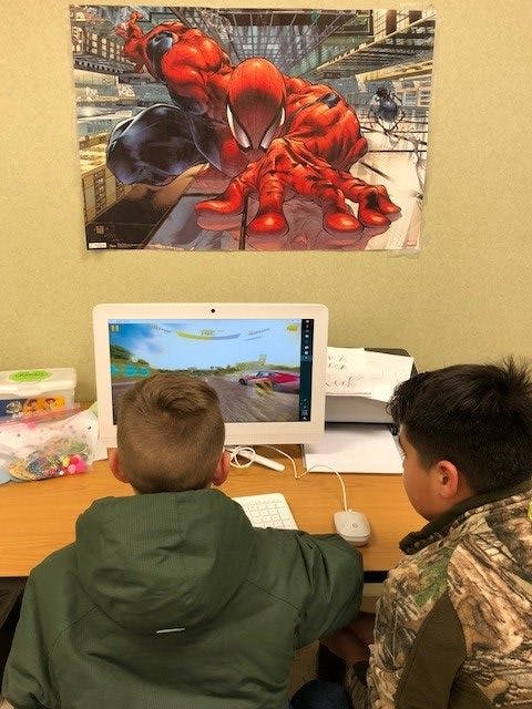 Two children looking at a computer screen with a Spider-Man poster above