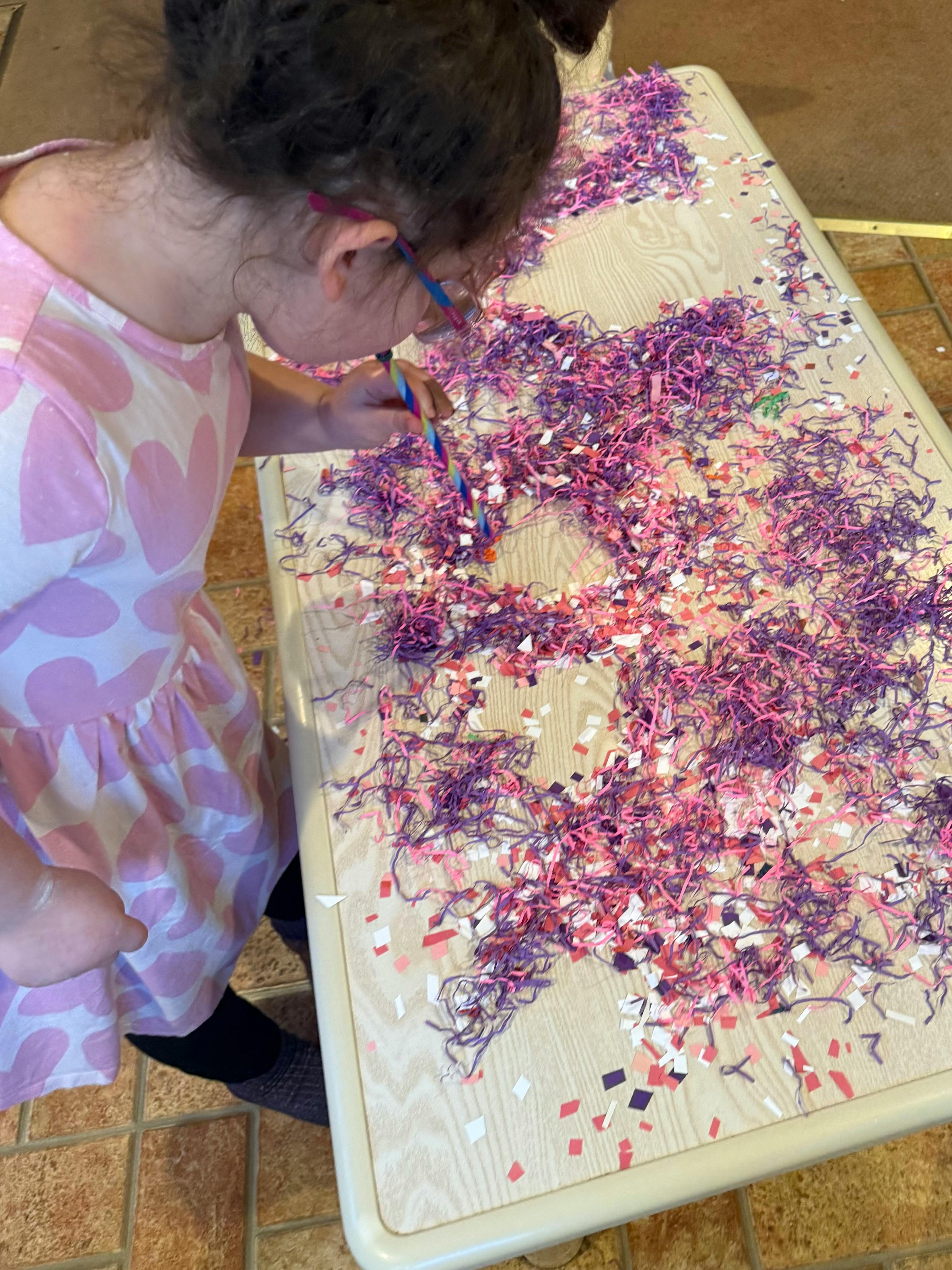 Child playing with colorful shredded paper on a table