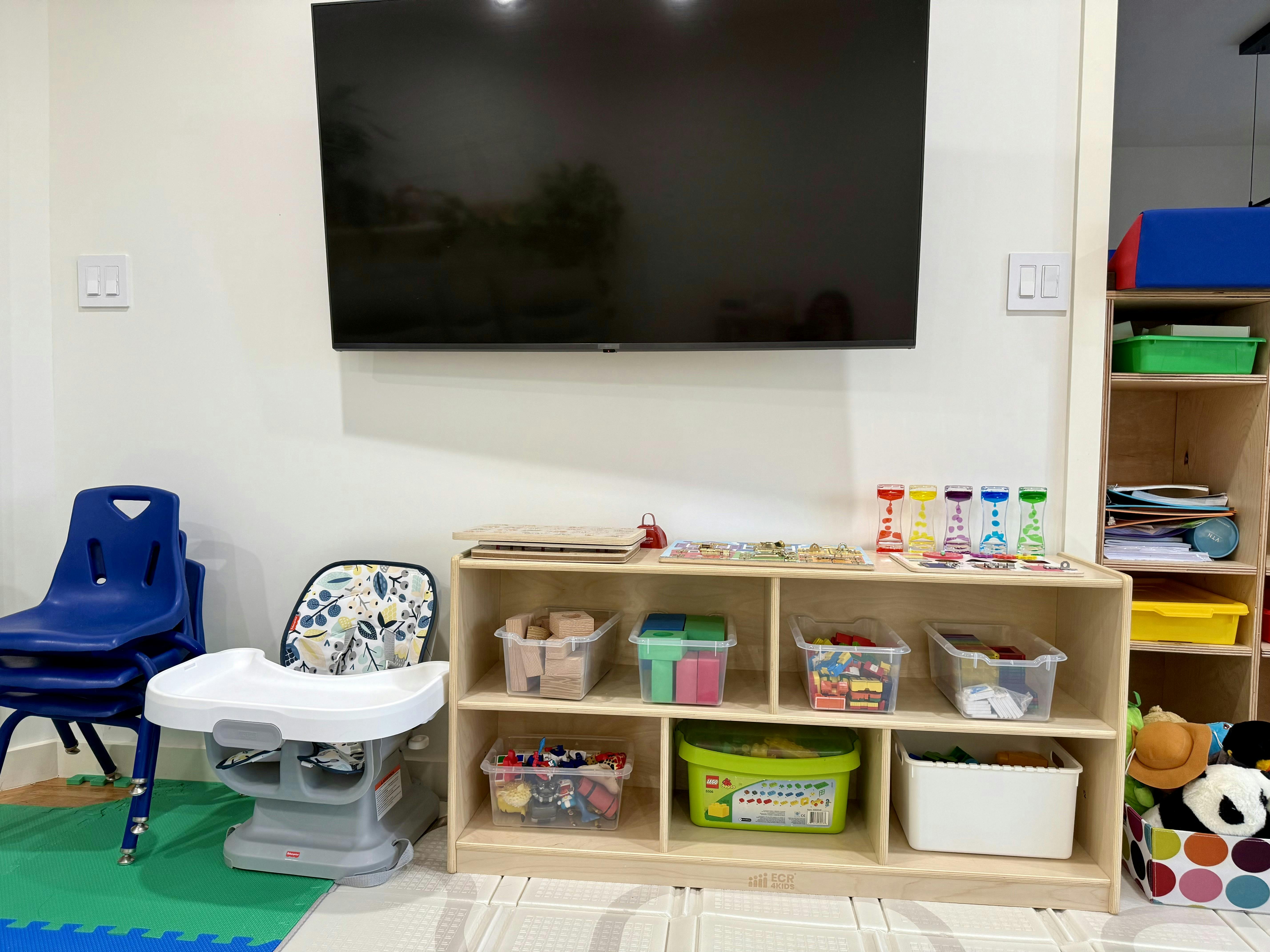 Child's high chair and blue chairs next to a wooden storage unit with toys