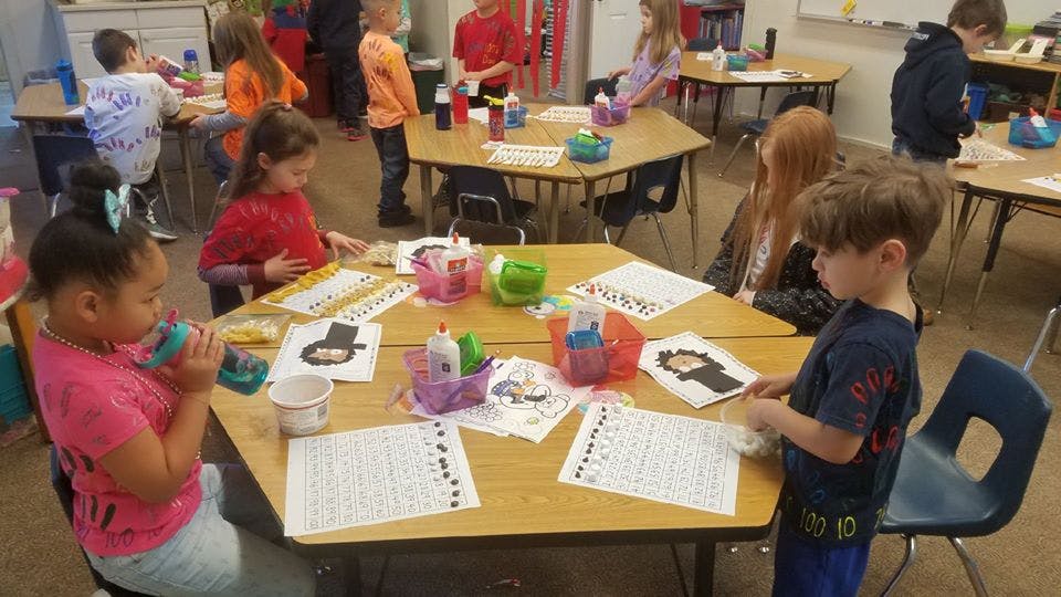 Children working on crafts at a hexagonal table in a classroom