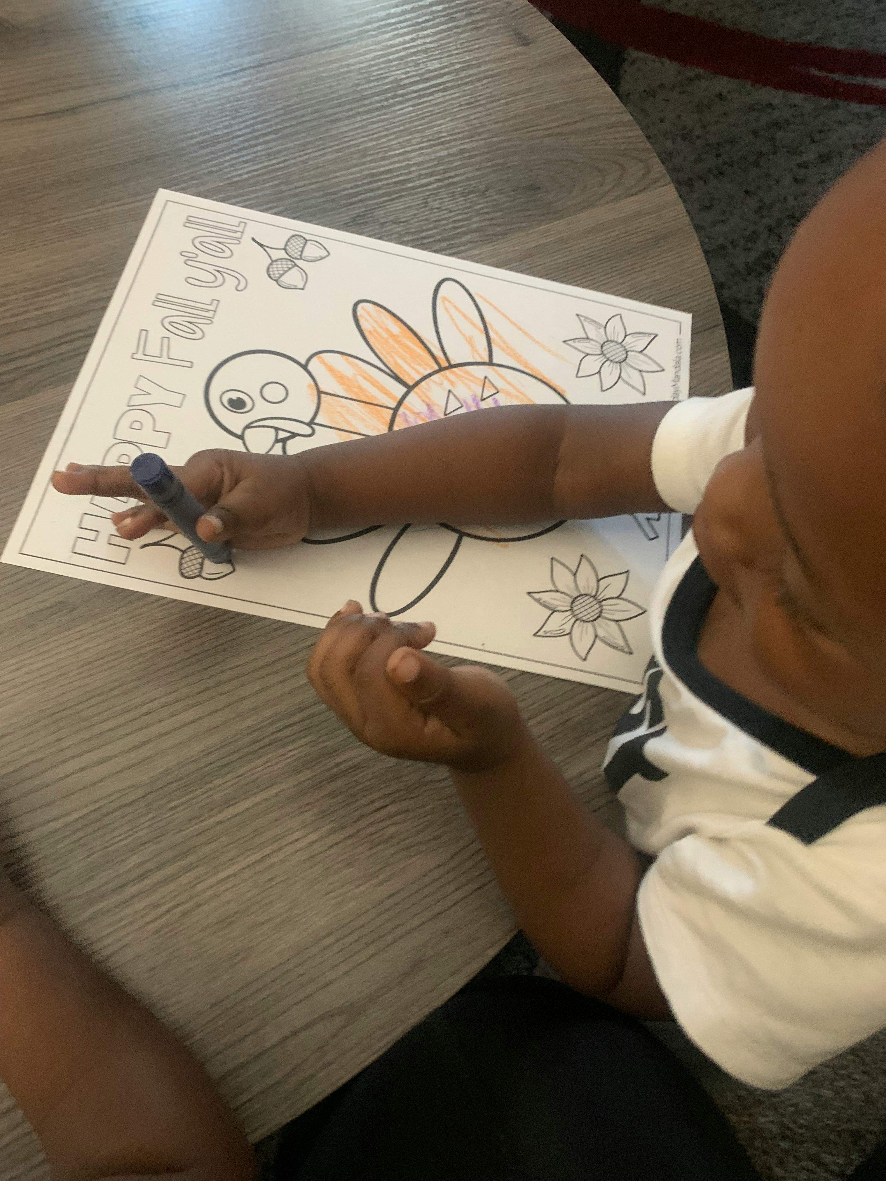 Child coloring a turkey on a coloring page that says "Happy Fall y'all"