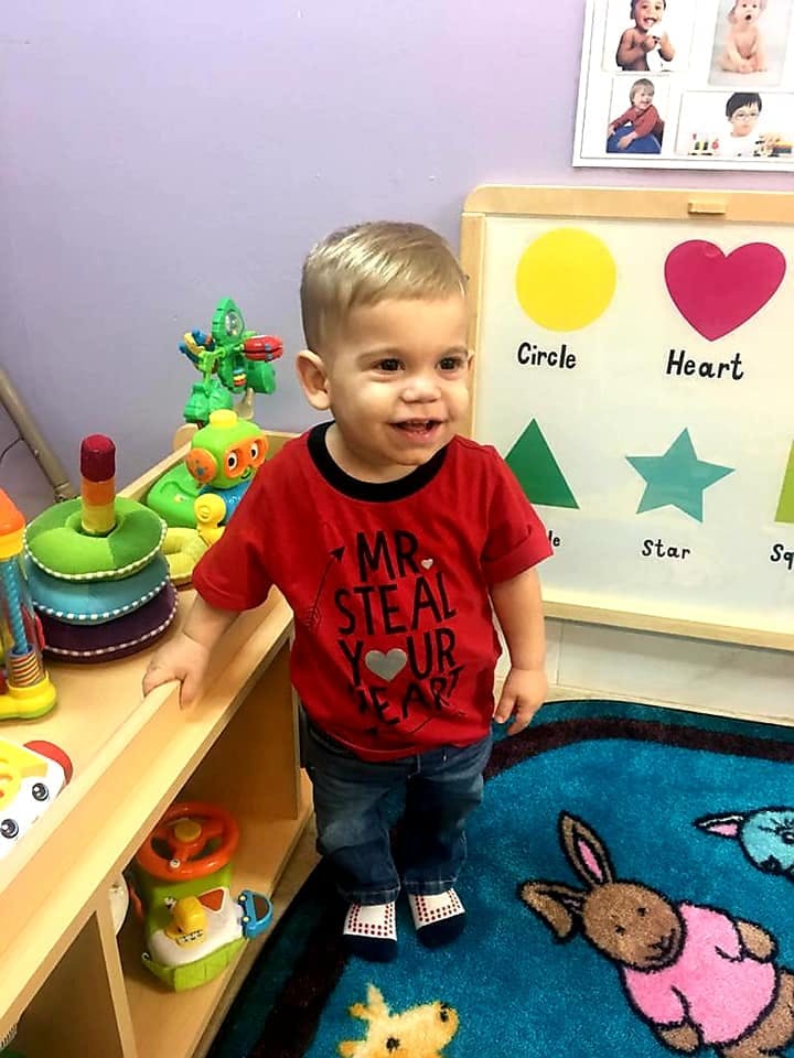 Child standing next to a shelf with toys and a whiteboard with shapes