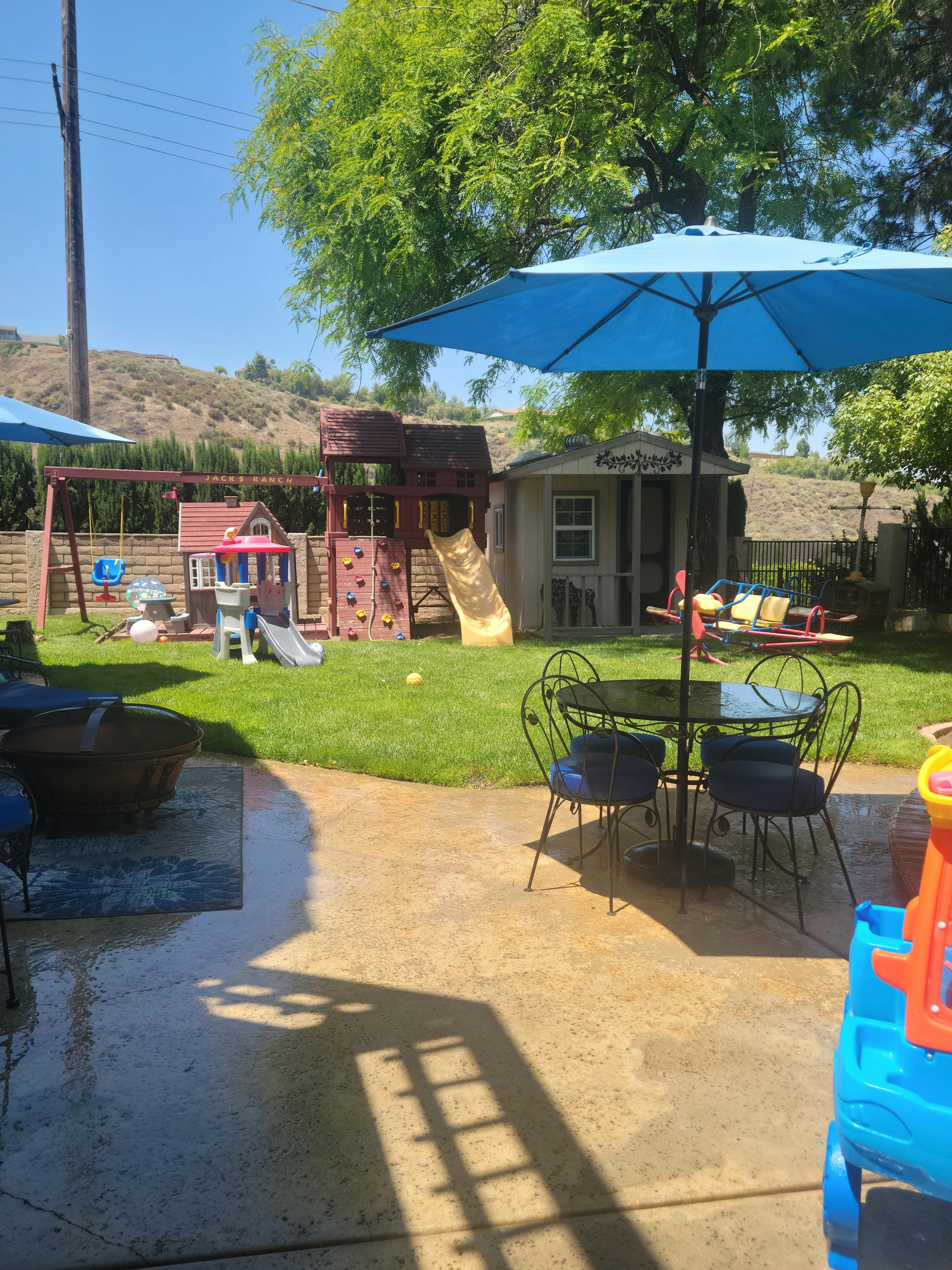 Backyard with a patio, blue umbrella, and a playground set on grass