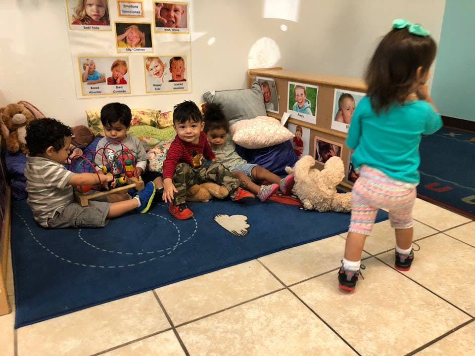 Children playing with toys on a blue rug in a classroom