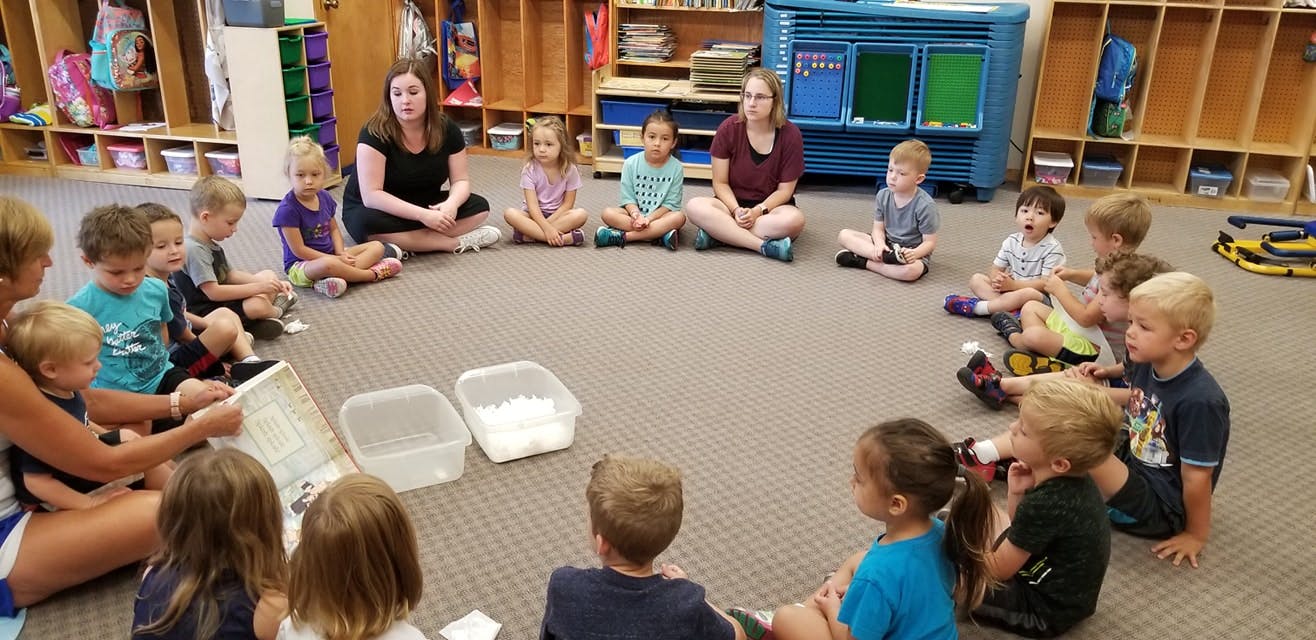 Adults and children sitting in a circle on the floor in a classroom