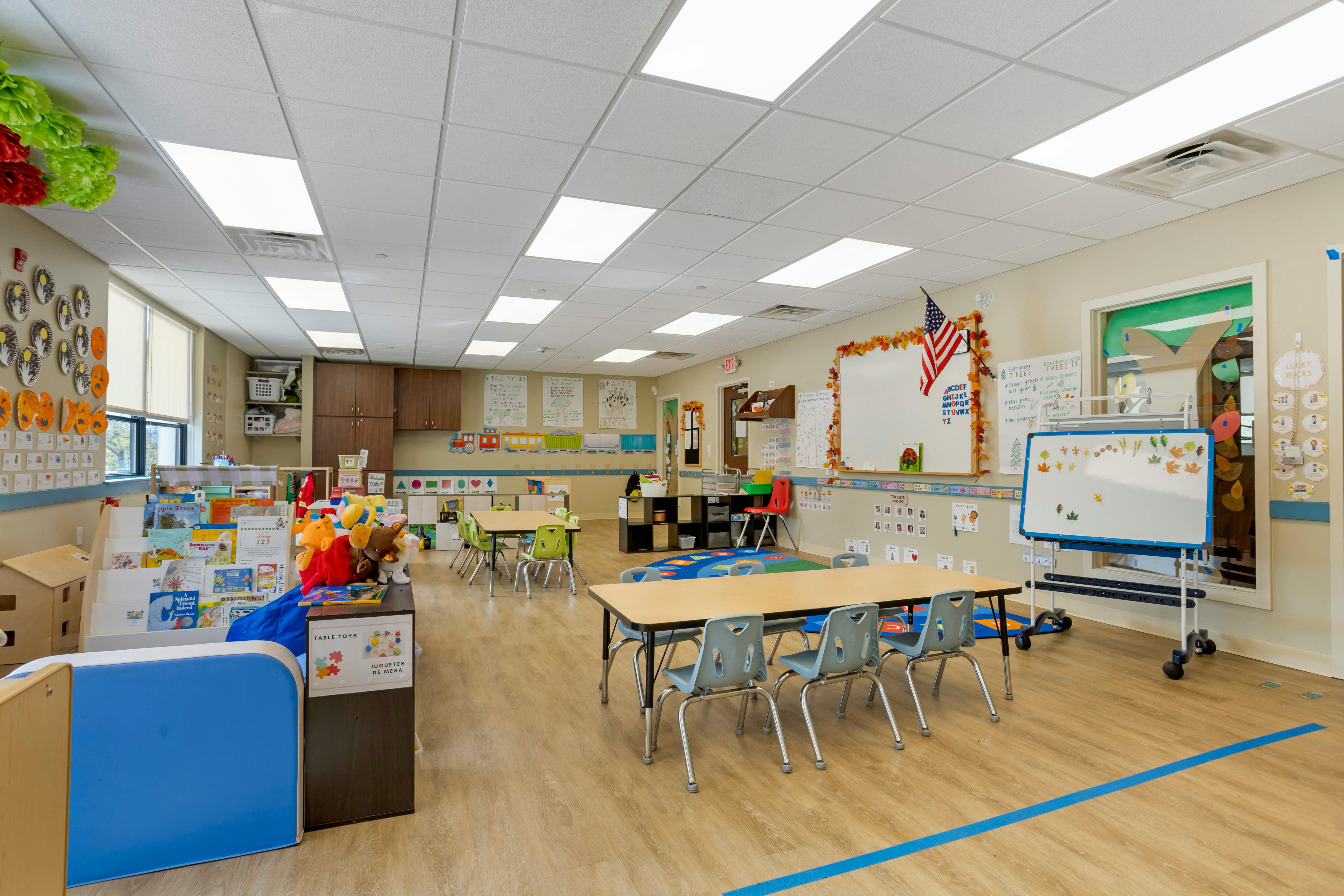 An empty early childhood classroom with small tables and chairs