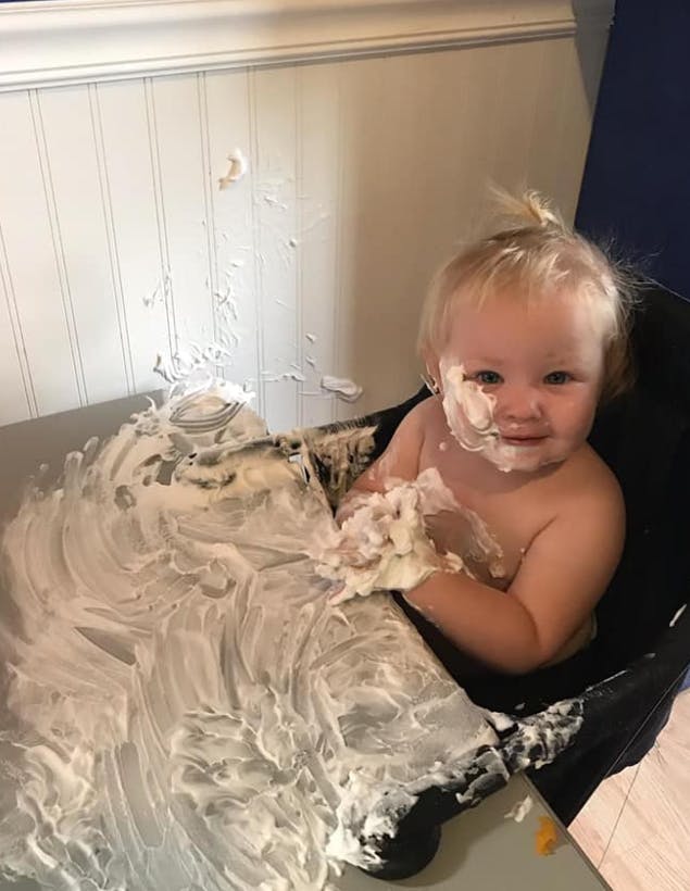 Child in a high chair covered in white cream