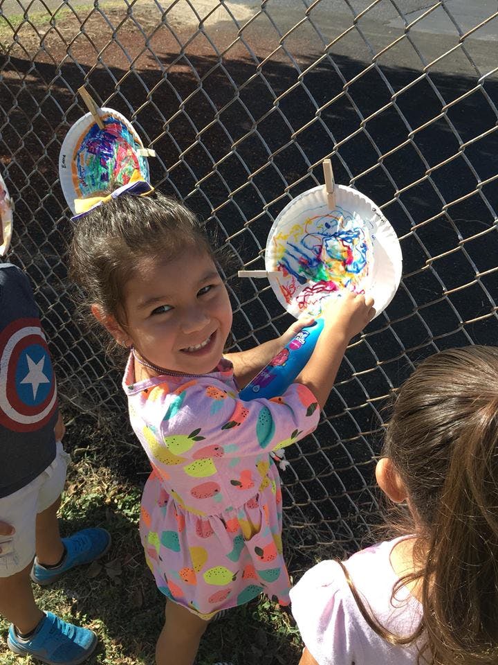 Child painting a paper plate attached to a fence