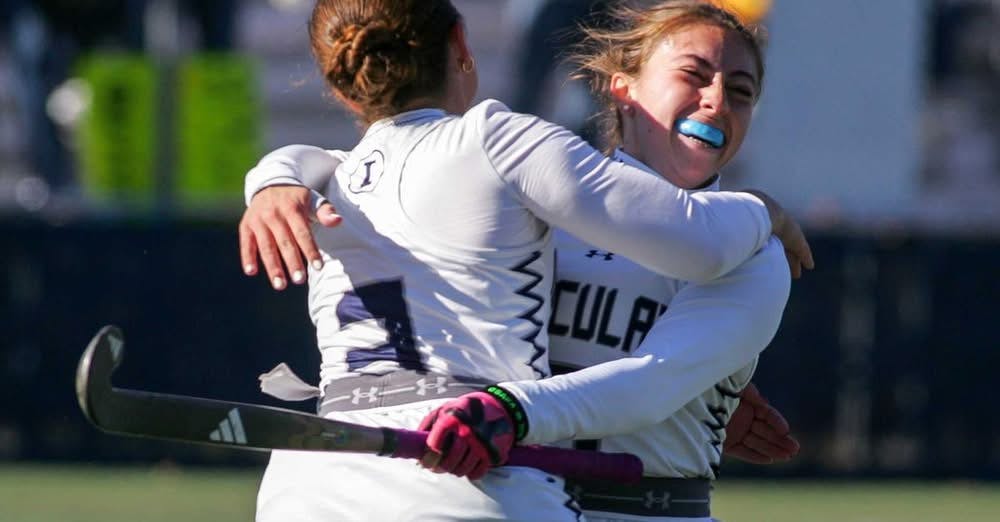 Field hockey players in white uniforms hugging on the field