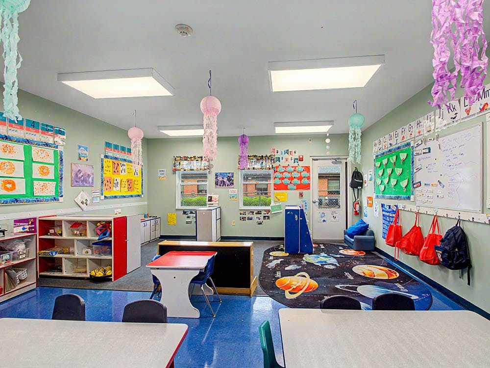 Classroom with children's art on walls, tables, and a space-themed rug
