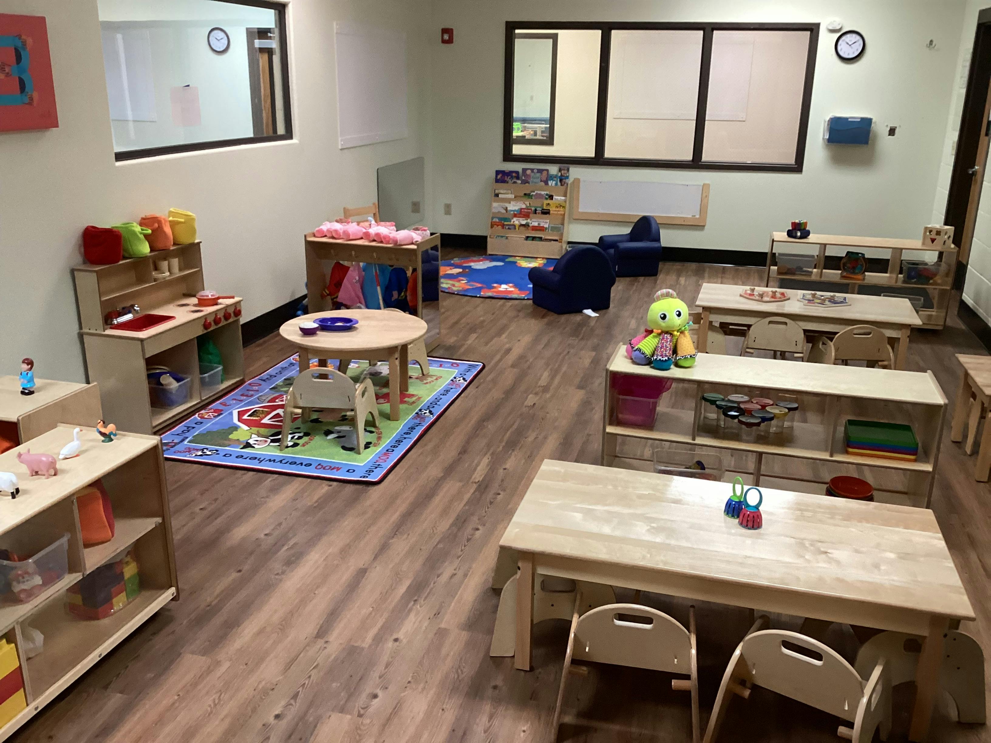 An empty children's playroom with tables, chairs, and cubbies full of toys
