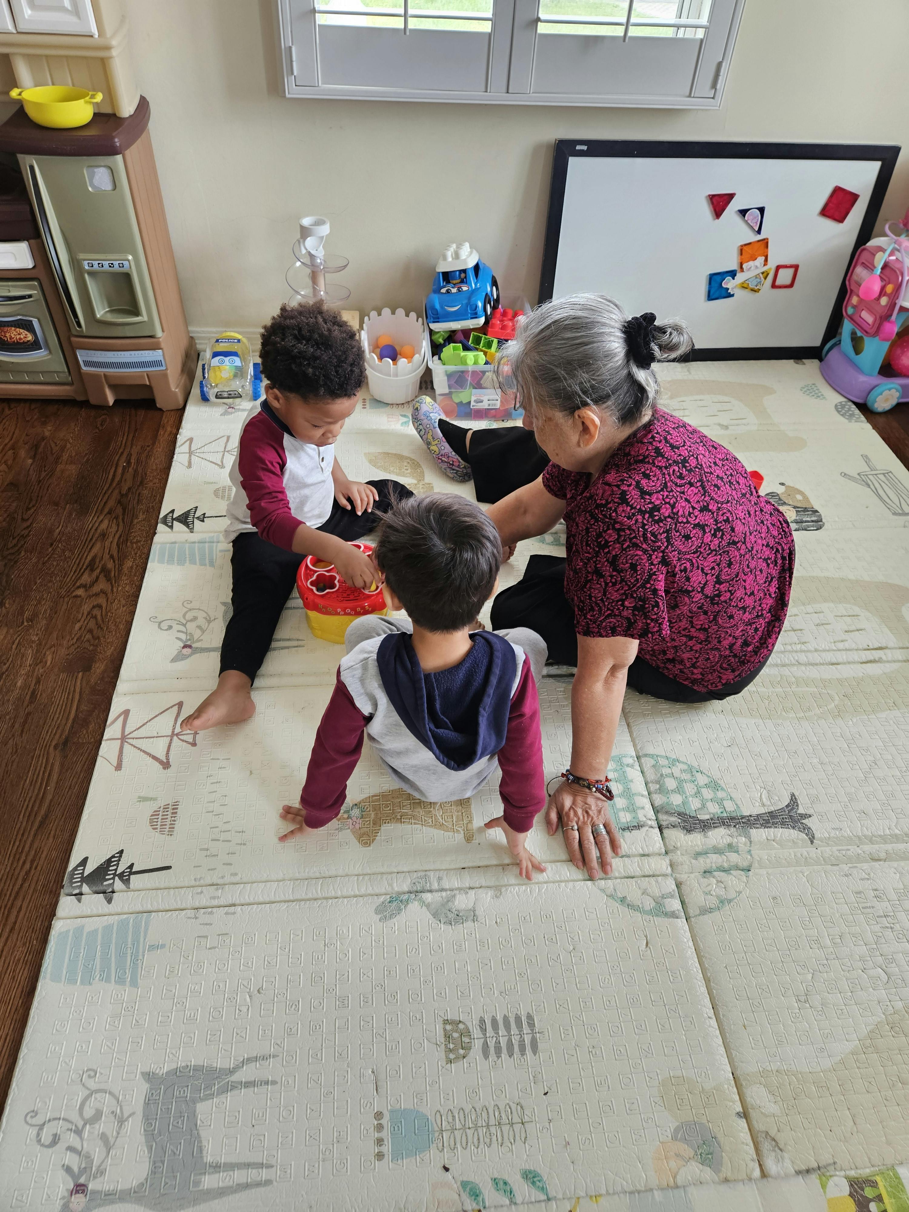 An adult and two children playing with toys on a mat