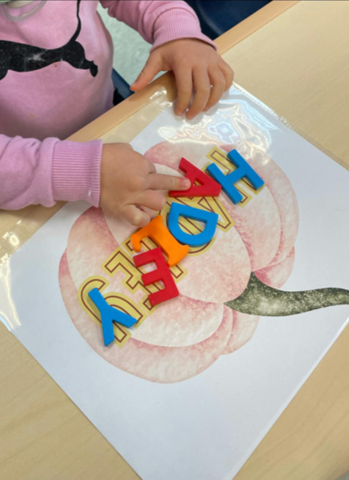 Child's hands arranging colorful letter magnets on a pumpkin drawing