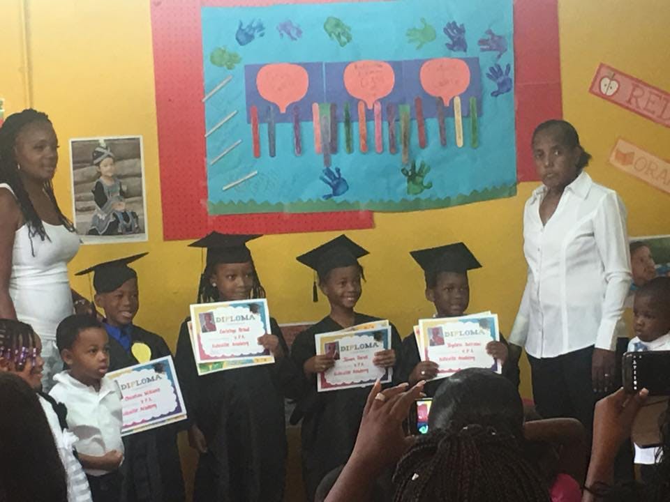 Children in graduation caps and gowns holding certificates with adults