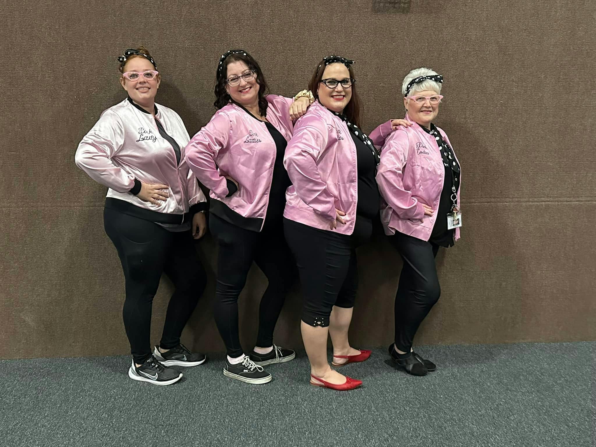 Four people posing in matching pink jackets and polka dot headbands