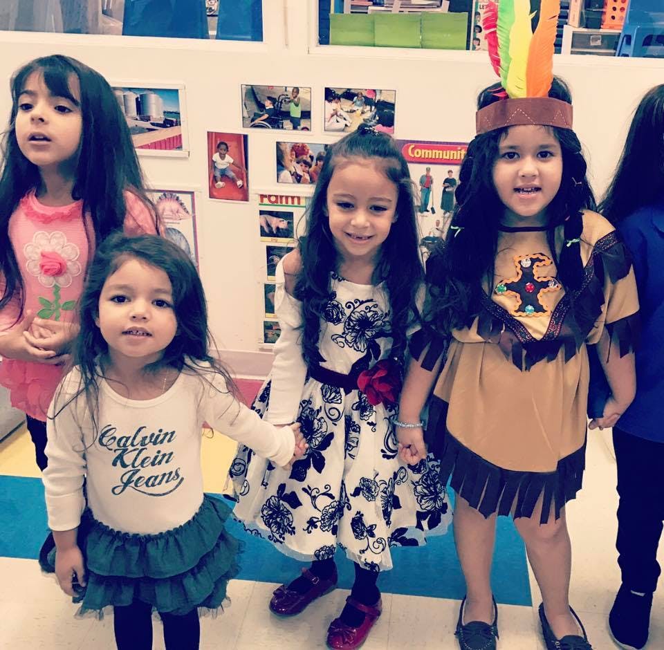 Four children standing, one in a feathered headband