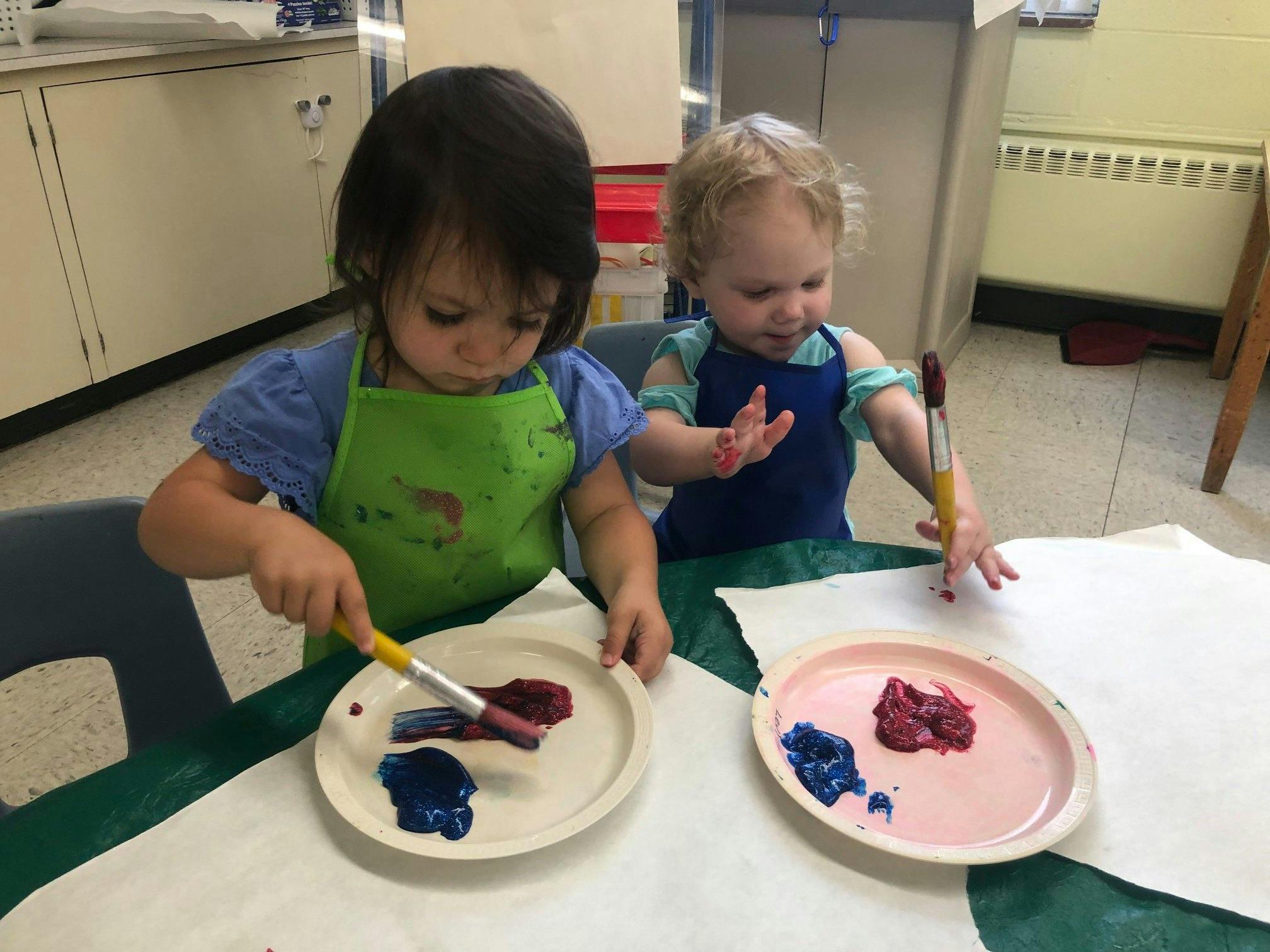 Two children painting with brushes and paint on plates