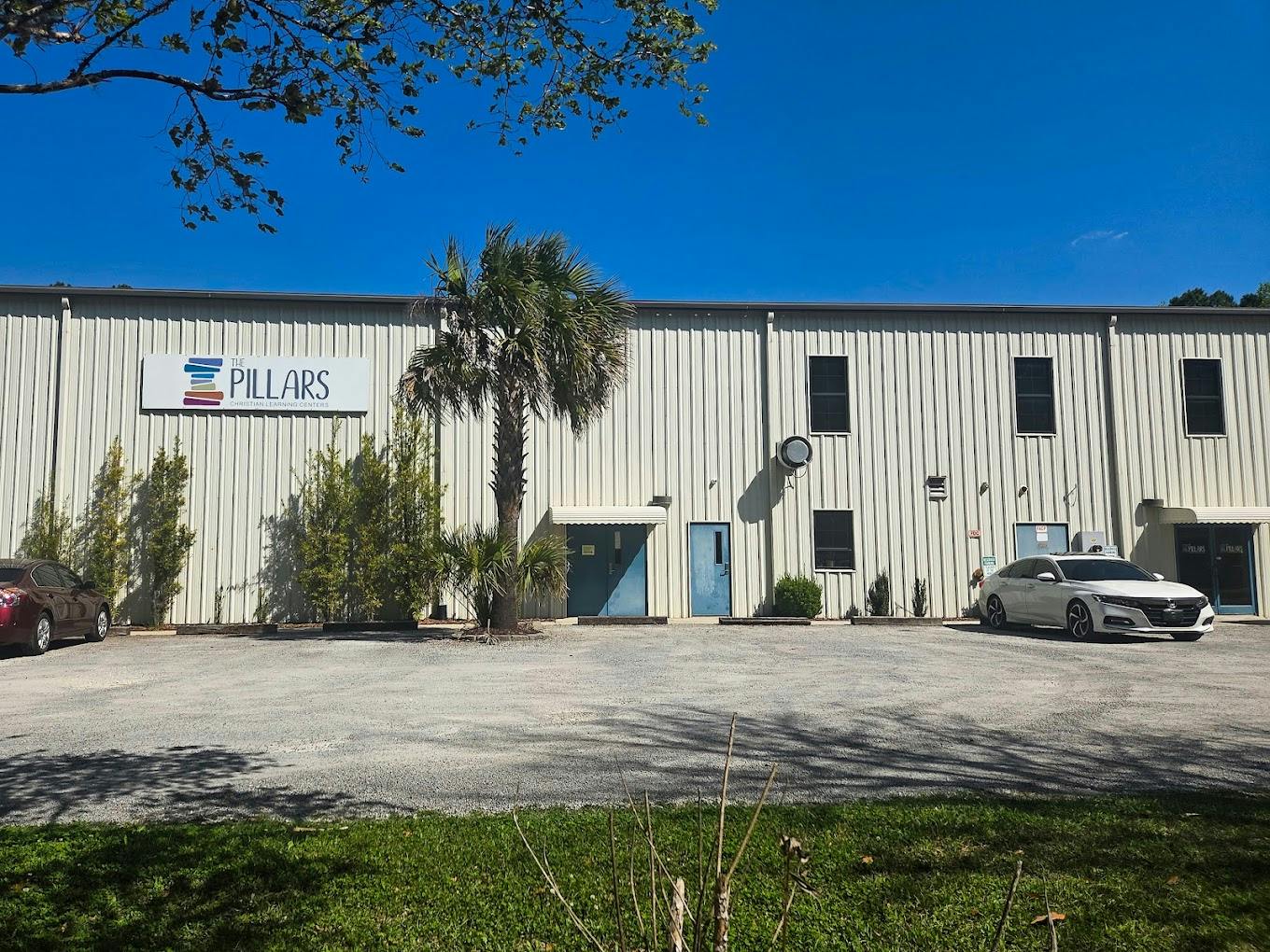 Exterior of The Pillars Christian Learning Centers building with cars parked