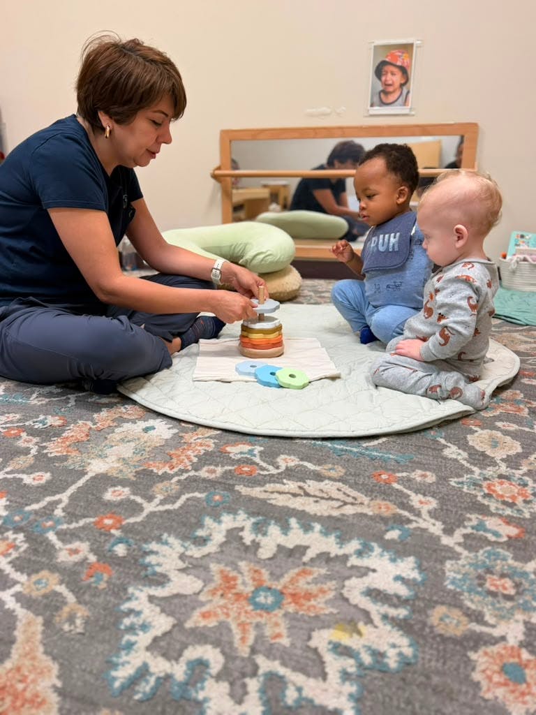 Adult and two children playing with a stacking ring toy on a rug