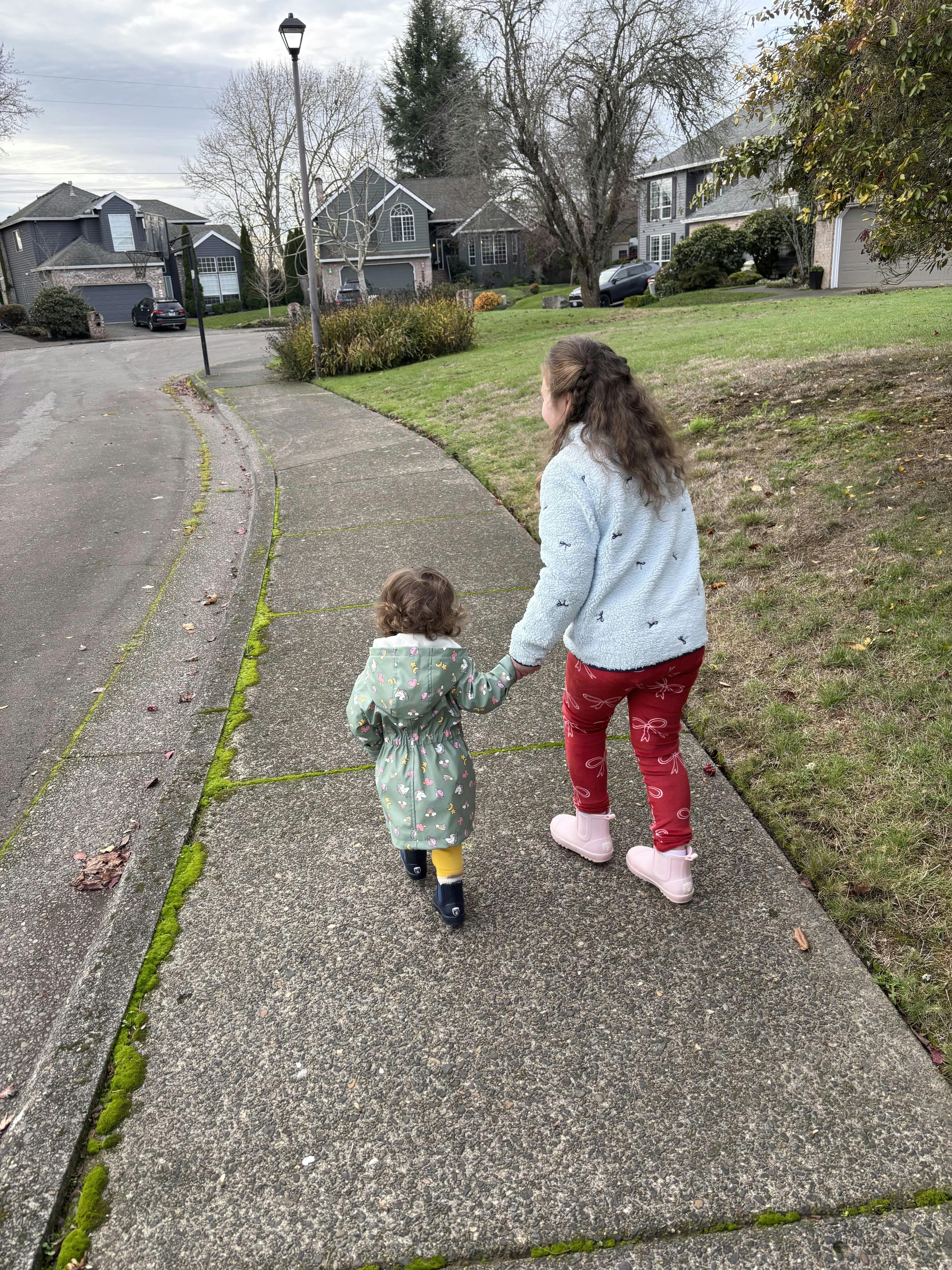 Child and person holding hands walking on a sidewalk