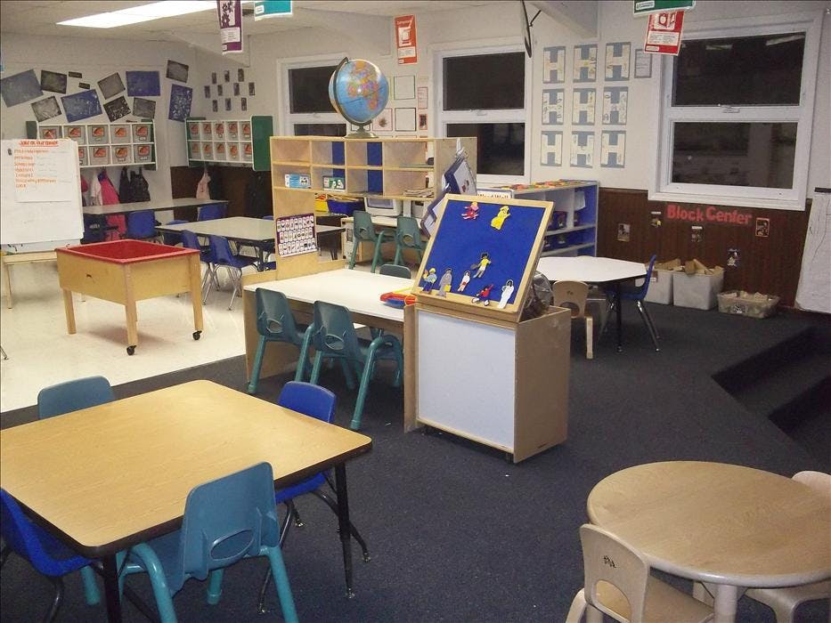 Classroom with child-sized tables and chairs, a sand table, and a felt board