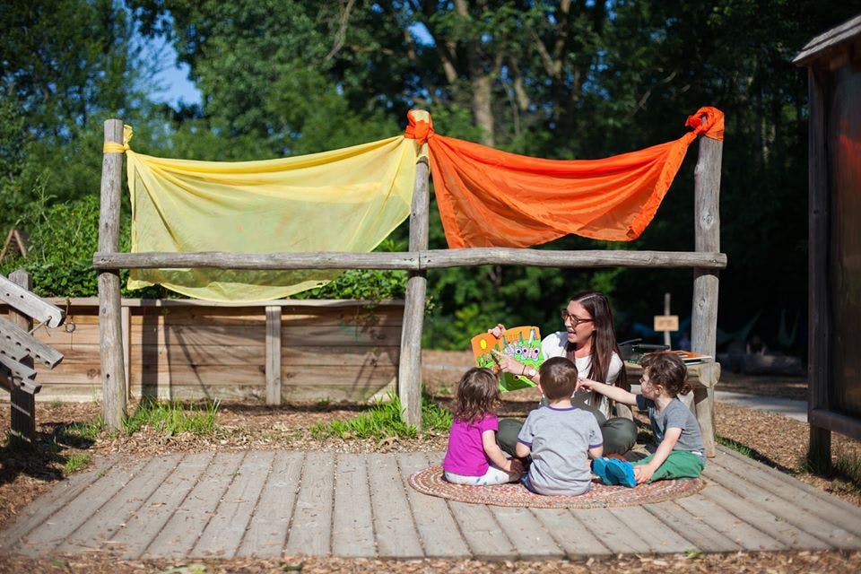 Person reading to three children outdoors