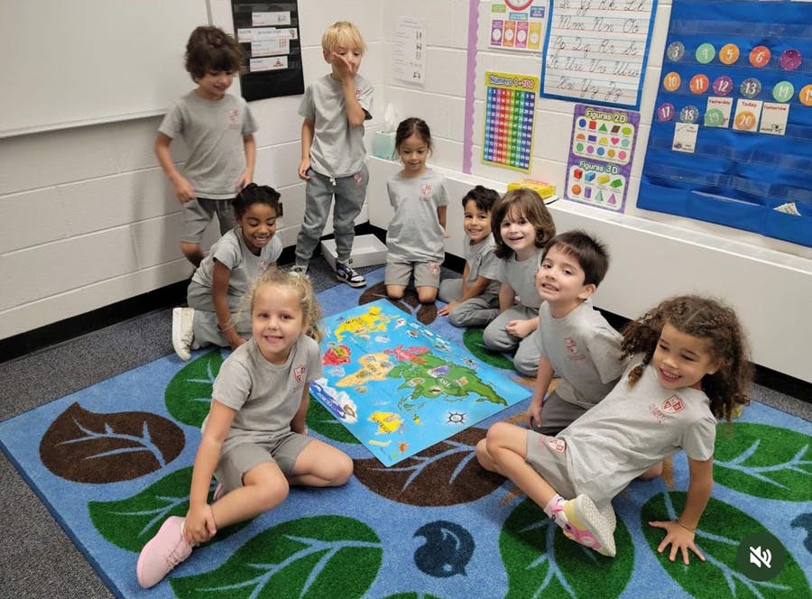 Group of children gathered around a world map on a rug in a classroom