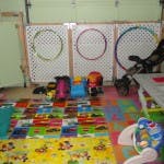 Play area with colorful mat, toys, and three hoops on a white fence