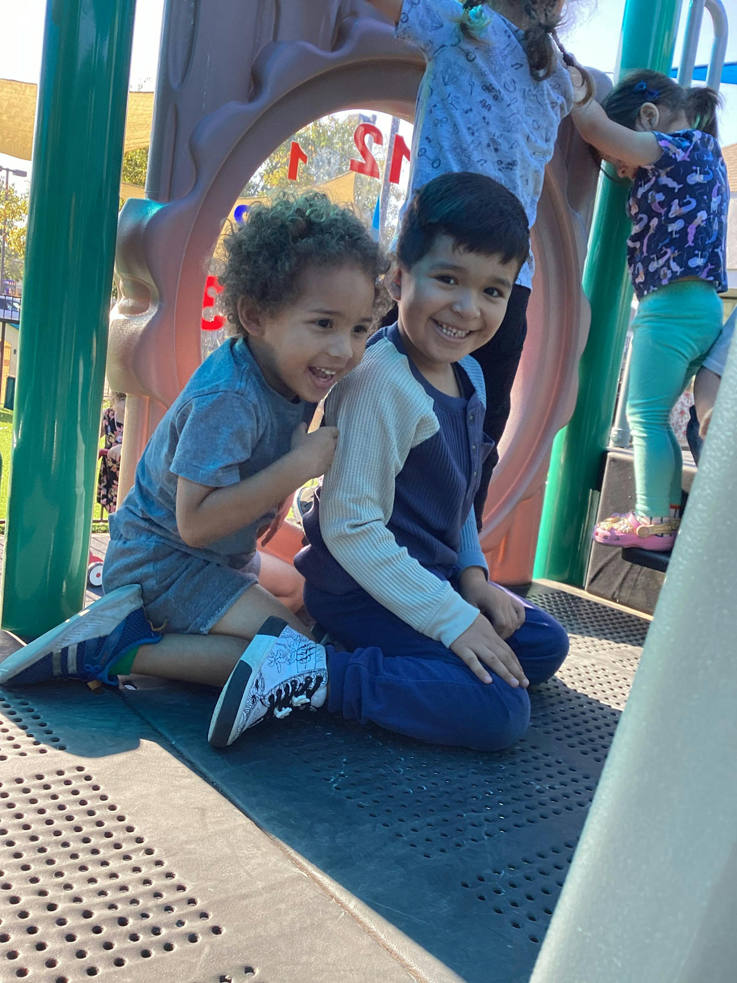 Two children smiling on playground equipment