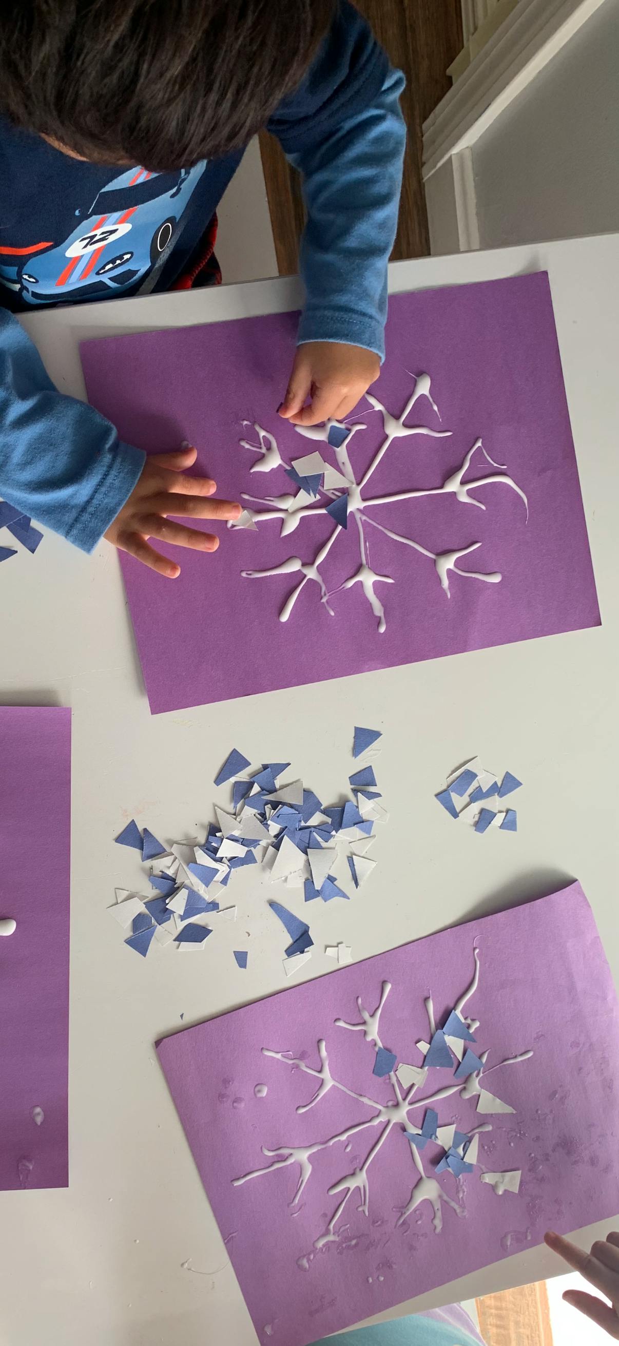 Child's hands creating a snowflake craft with glue and paper pieces