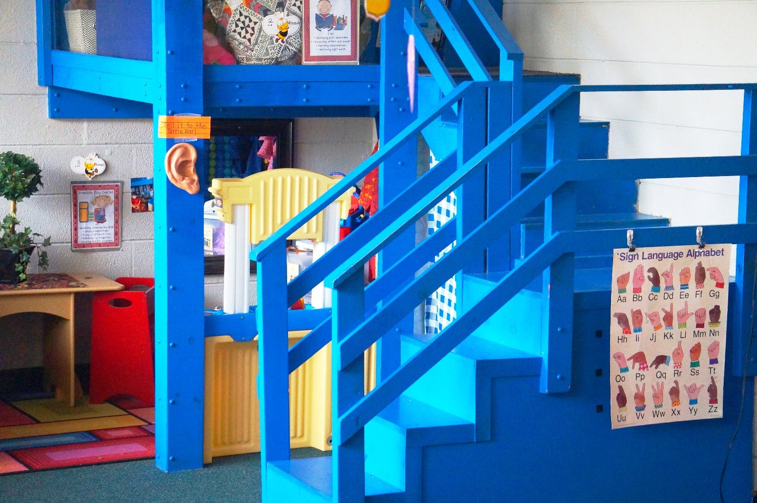 Blue wooden play structure with stairs and a sign language chart