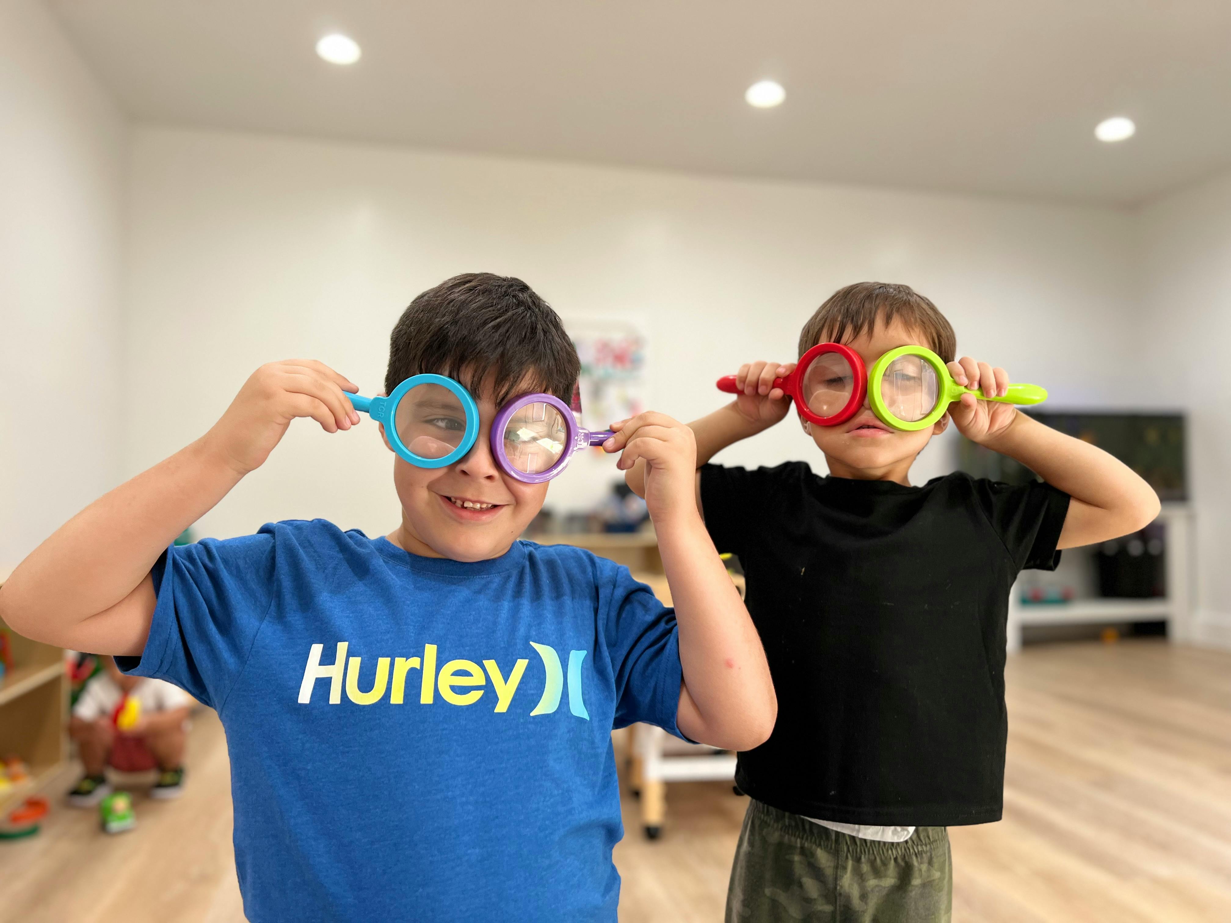 Two children holding magnifying glasses over their eyes