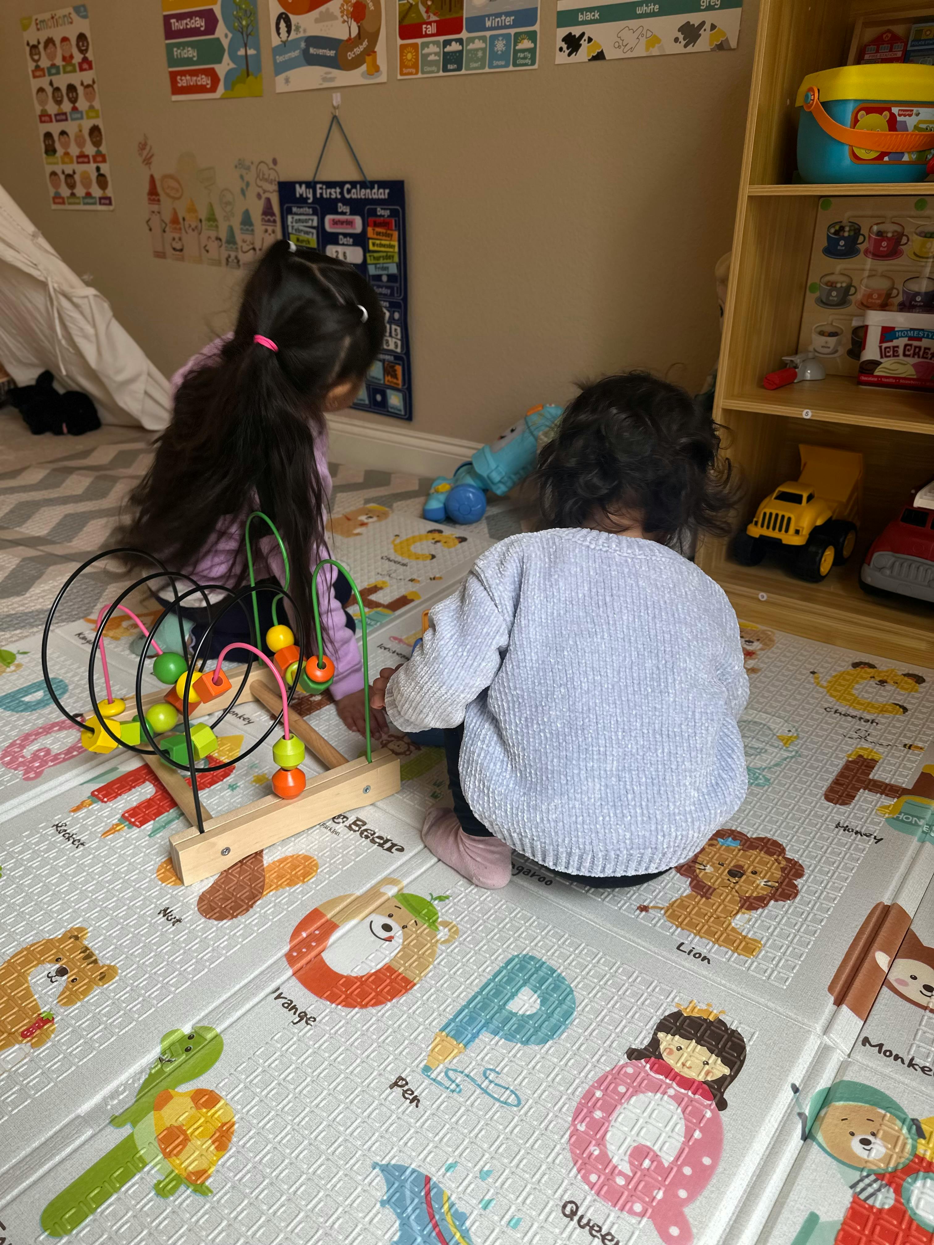 Two children playing with a bead maze toy on an alphabet mat