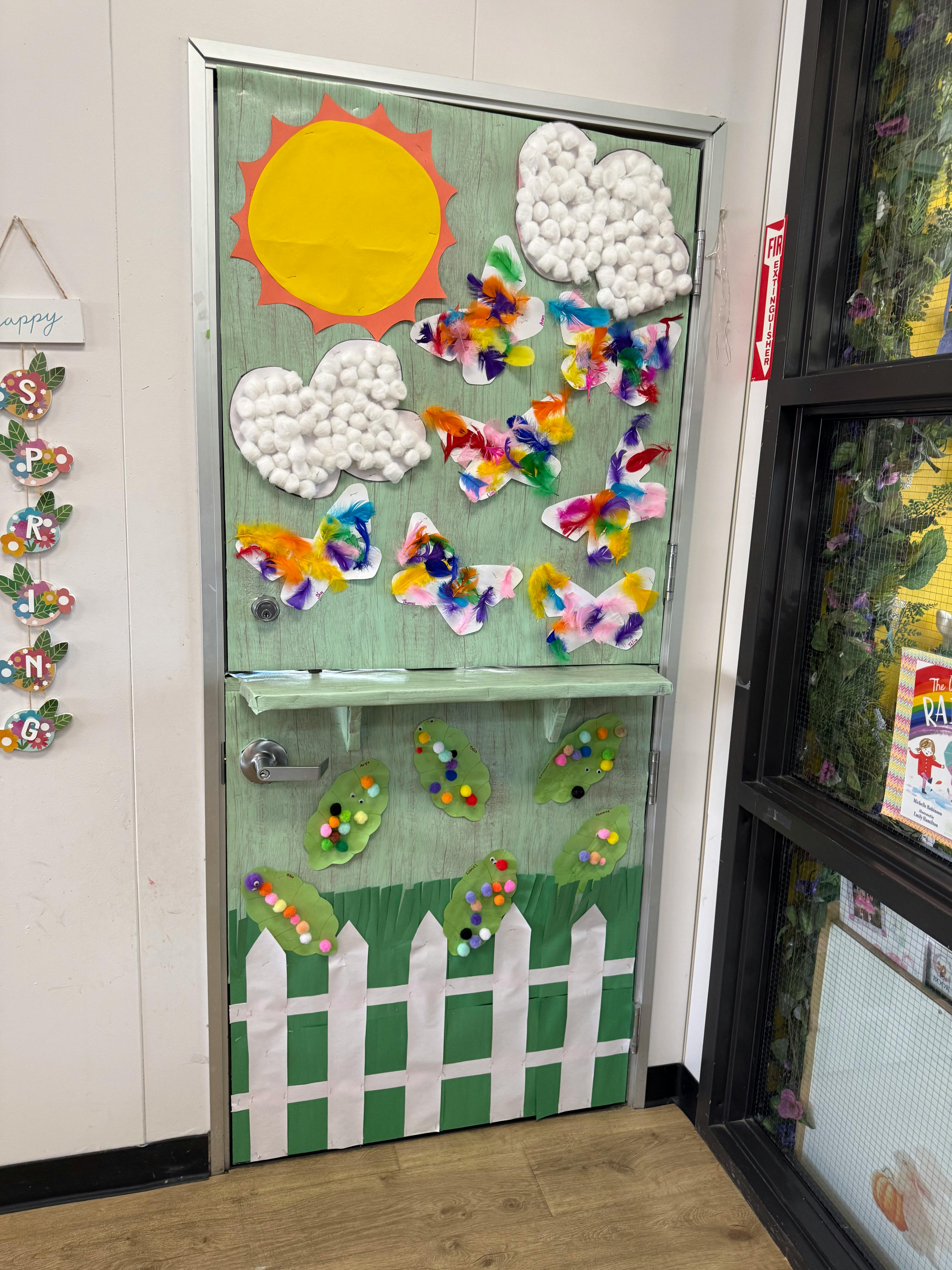 Classroom door decorated with craft butterflies, sun, clouds, and caterpillars